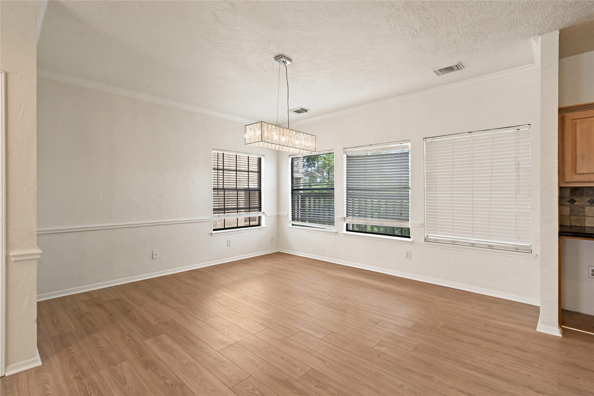2607 Sailboat Drive, Houston, TX 77058 Bright dining area with elegant wood flooring, large windows for natural light, and a modern chandelier, offering a perfect space for gatherings.