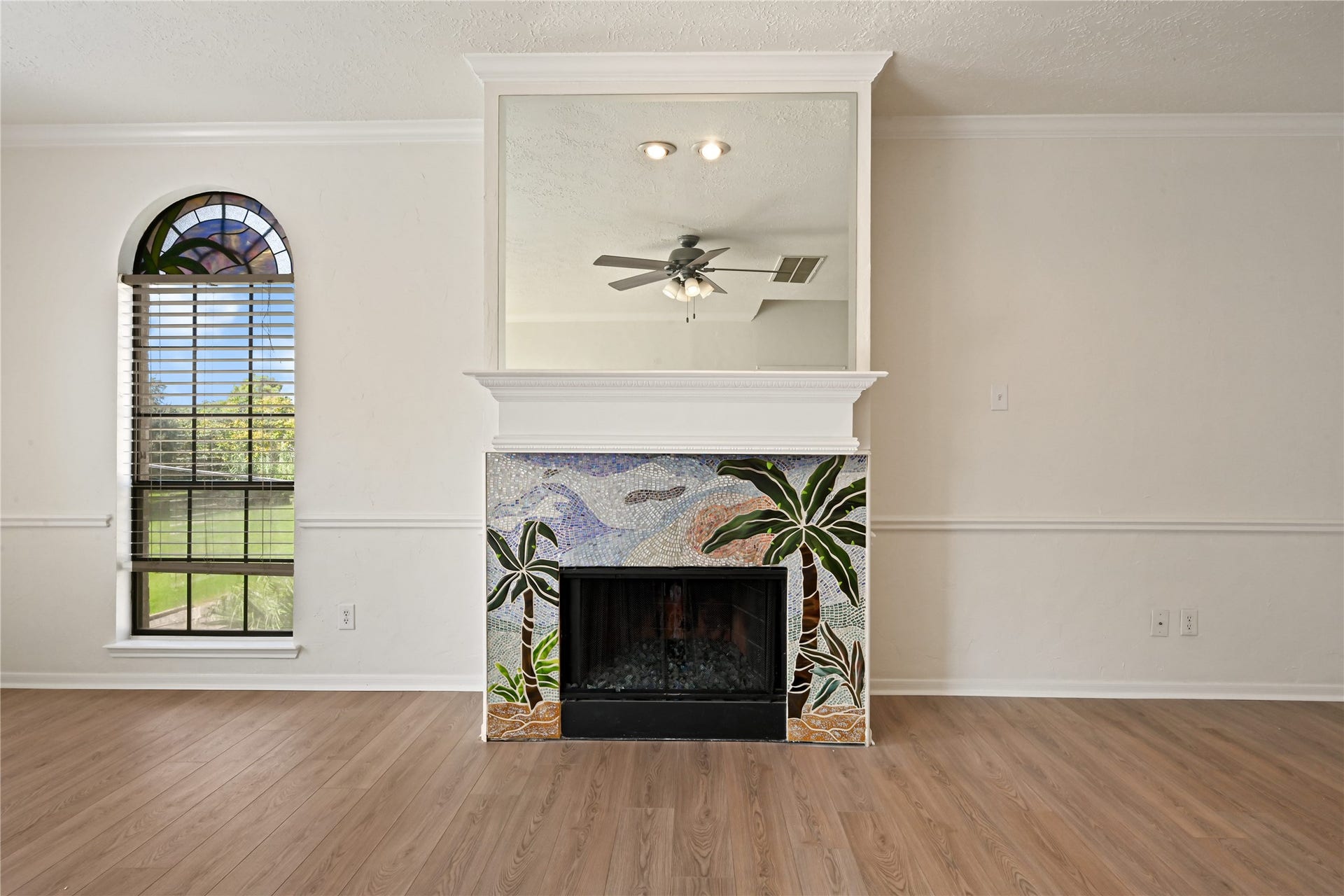 2607 Sailboat Drive, Houston, TX 77058 Inviting living space featuring a unique mosaic-tiled fireplace with a tropical motif, complemented by elegant wood flooring and a stylish arched window that lets in abundant natural light.