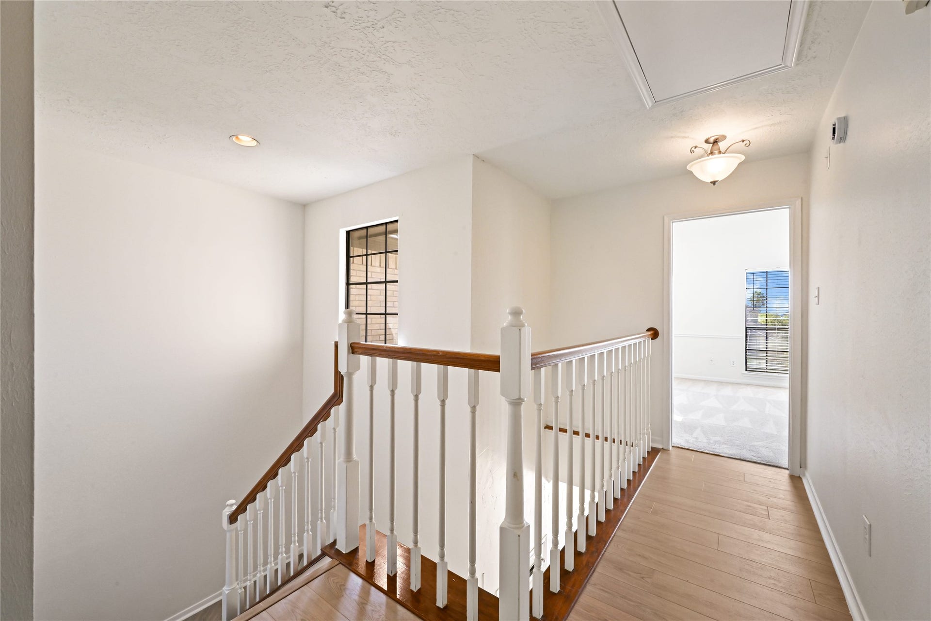 2607 Sailboat Drive, Houston, TX 77058 Bright and airy upstairs landing with elegant wood flooring and a classic railing, leading to a well-lit room with large windows.