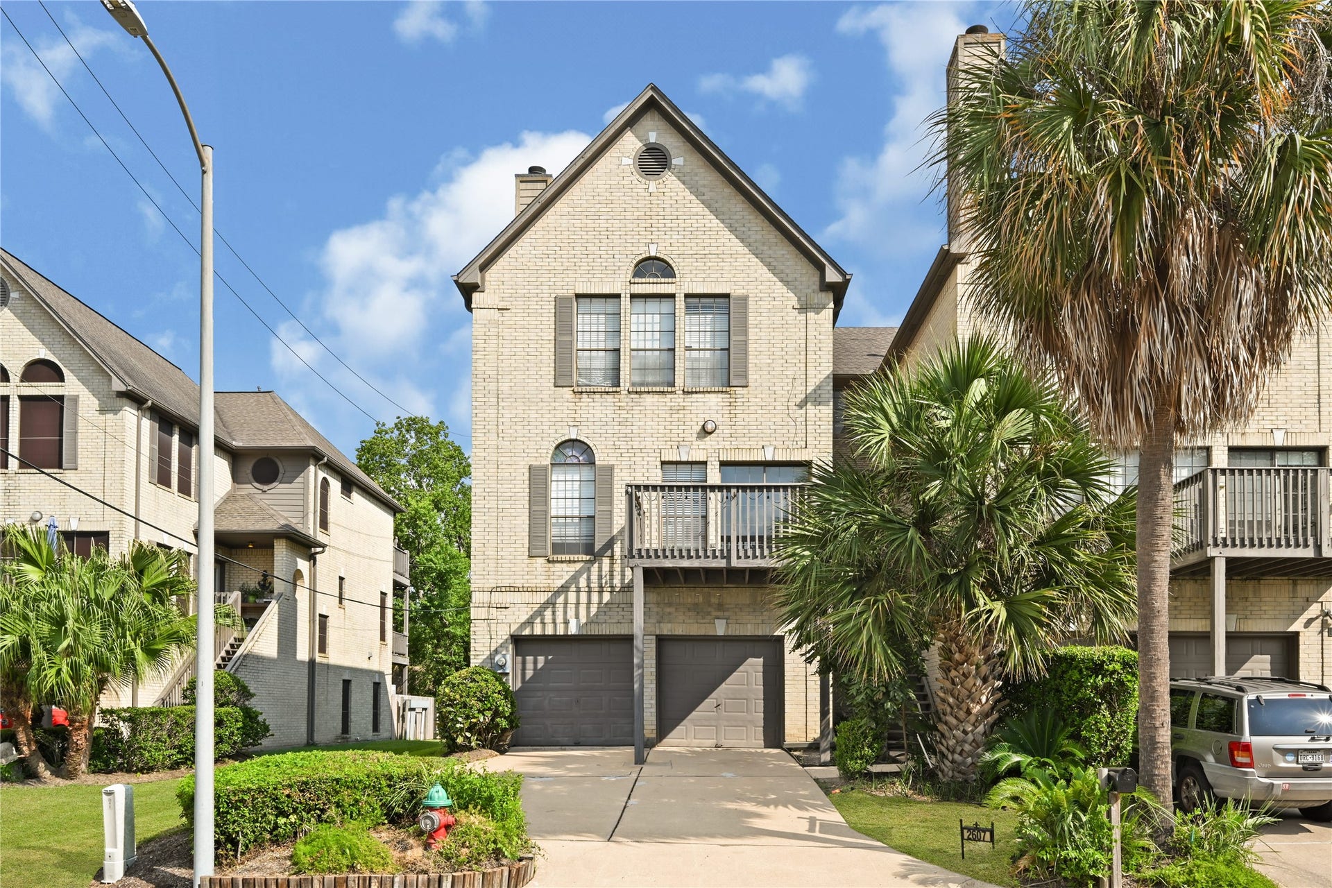2607 Sailboat Drive, Houston, TX 77058 Charming multi-level townhouse with a brick exterior, featuring a spacious two-car garage and lush palm landscaping, set in a serene neighborhood.