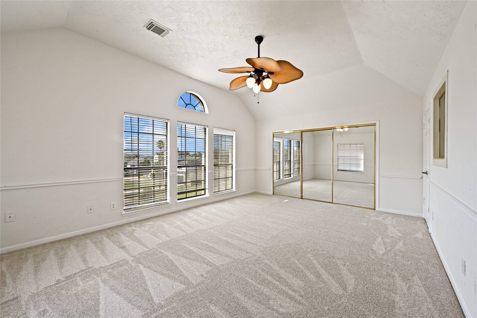 2607 Sailboat Drive, Houston, TX 77058 Spacious bedroom with vaulted ceiling, featuring large windows for ample natural light, plush carpeting, and mirrored closet doors for added elegance.