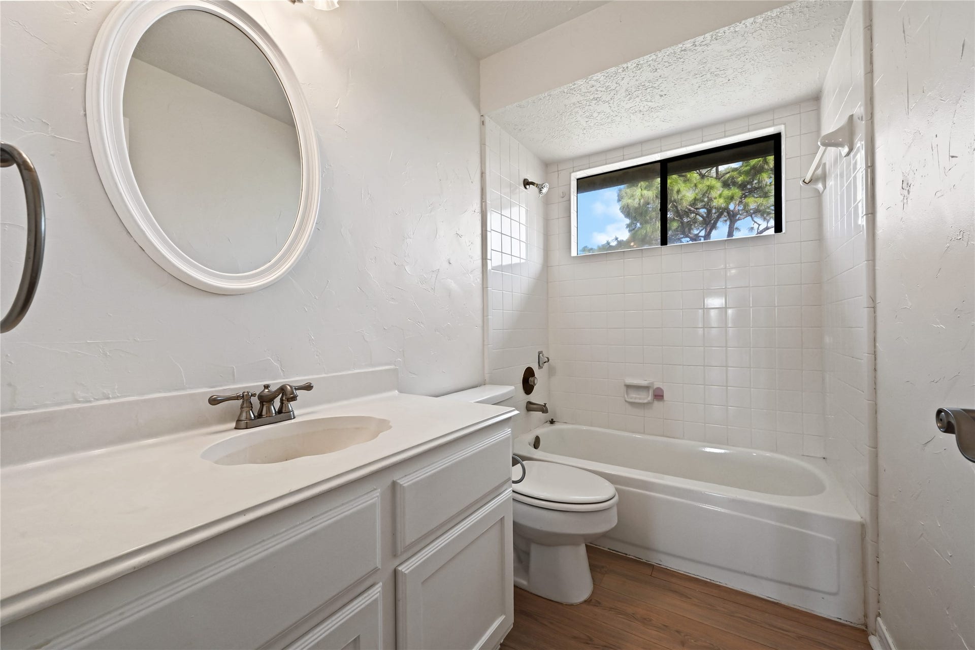 2607 Sailboat Drive, Houston, TX 77058 Bright and airy bathroom featuring a sleek white vanity, a classic bathtub with a window view, and elegant wood flooring.