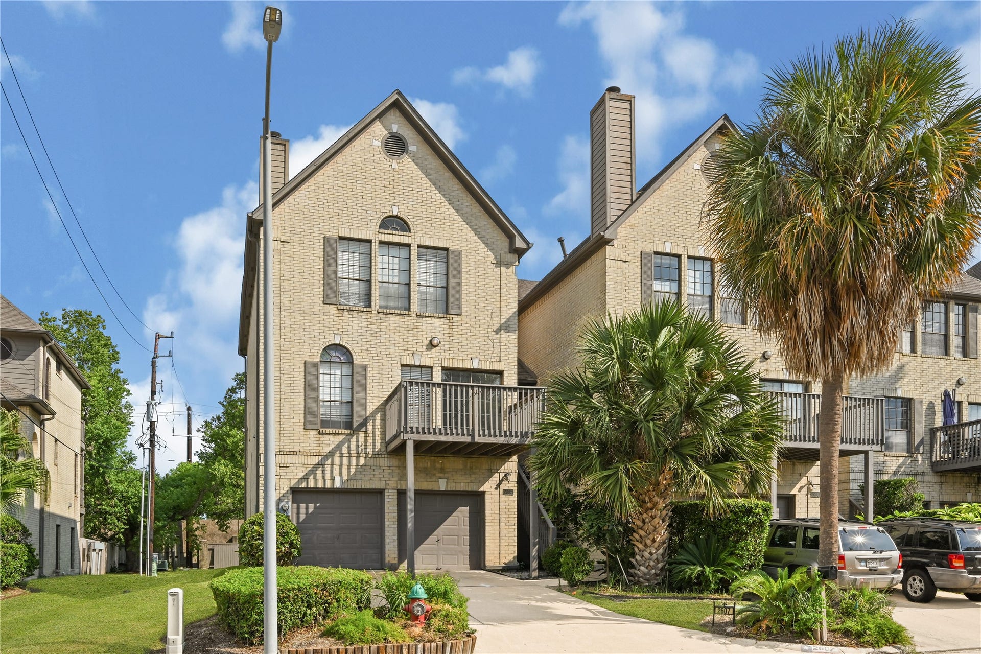 2607 Sailboat Drive, Houston, TX 77058 Charming townhouse with a brick exterior, featuring a spacious deck and lush palm trees, offering a blend of elegance and tropical charm.