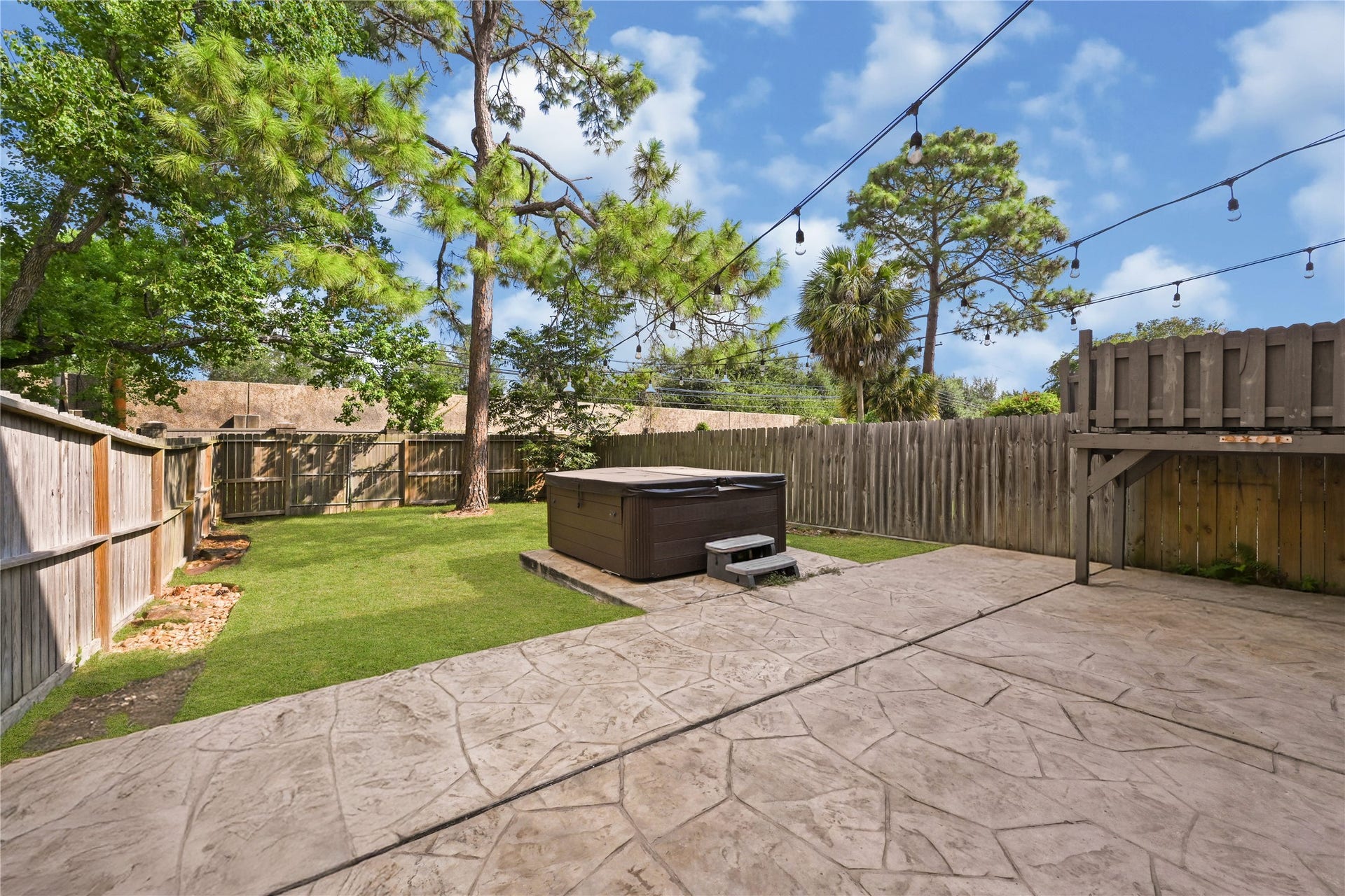 2607 Sailboat Drive, Houston, TX 77058 Charming backyard oasis featuring a spacious stamped concrete patio, a relaxing hot tub, and lush greenery surrounded by a privacy fence, perfect for outdoor entertaining.