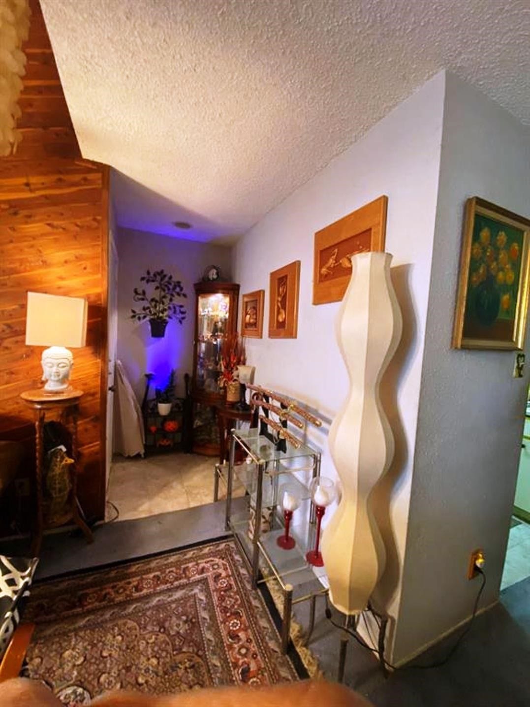 10049 Westpark Drive, #136, Houston, TX 77042 Cozy corner with a blend of wood and light-colored walls, featuring eclectic decor, including art pieces and a unique wavy lamp. The space has a warm, inviting ambiance, enhanced by soft lighting and a decorative rug.