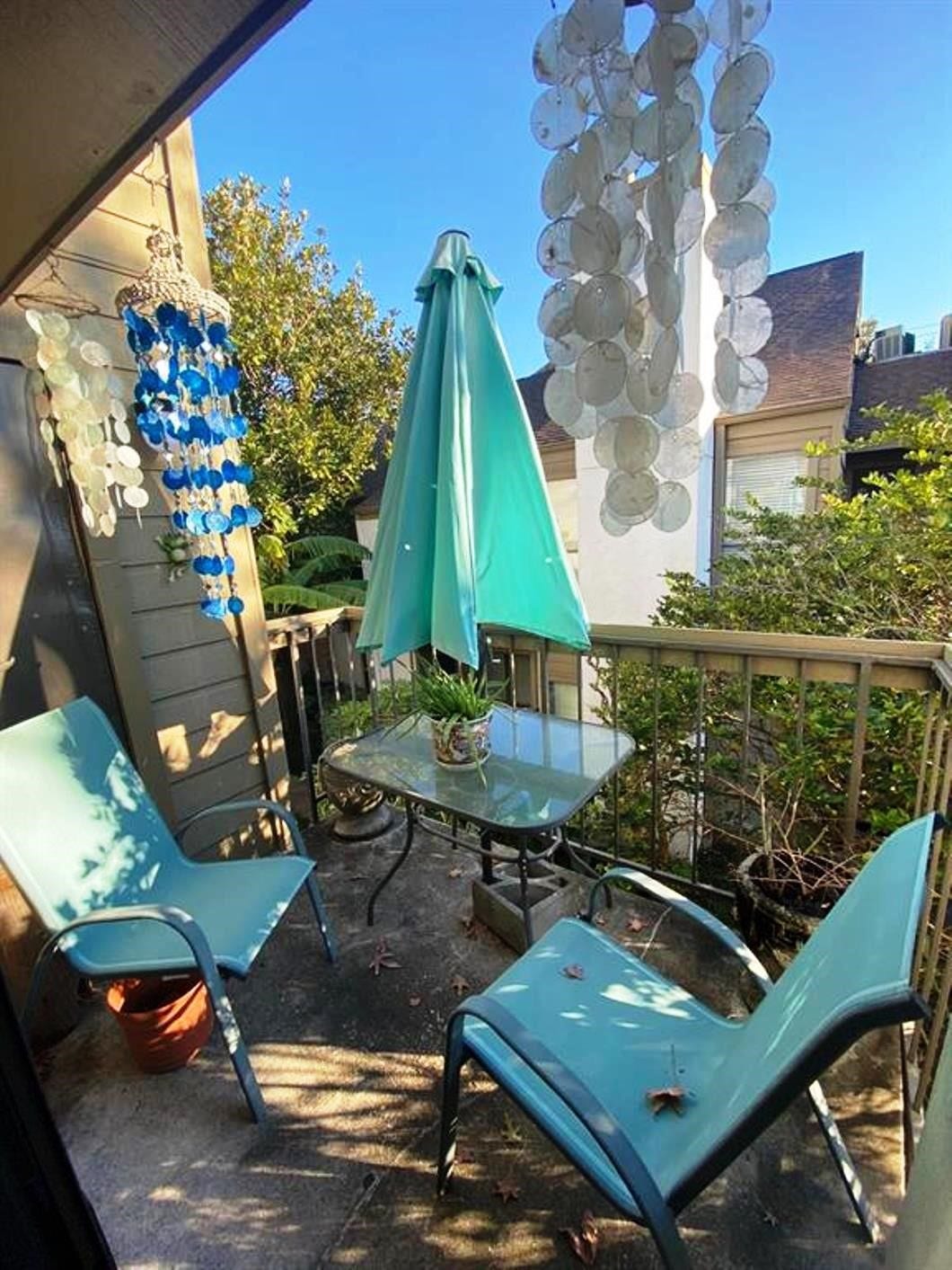 10049 Westpark Drive, #136, Houston, TX 77042 Cozy balcony with two chairs and a small glass table, perfect for relaxing. Decor includes hanging blue and white ornaments and a teal umbrella, creating a tranquil outdoor retreat.