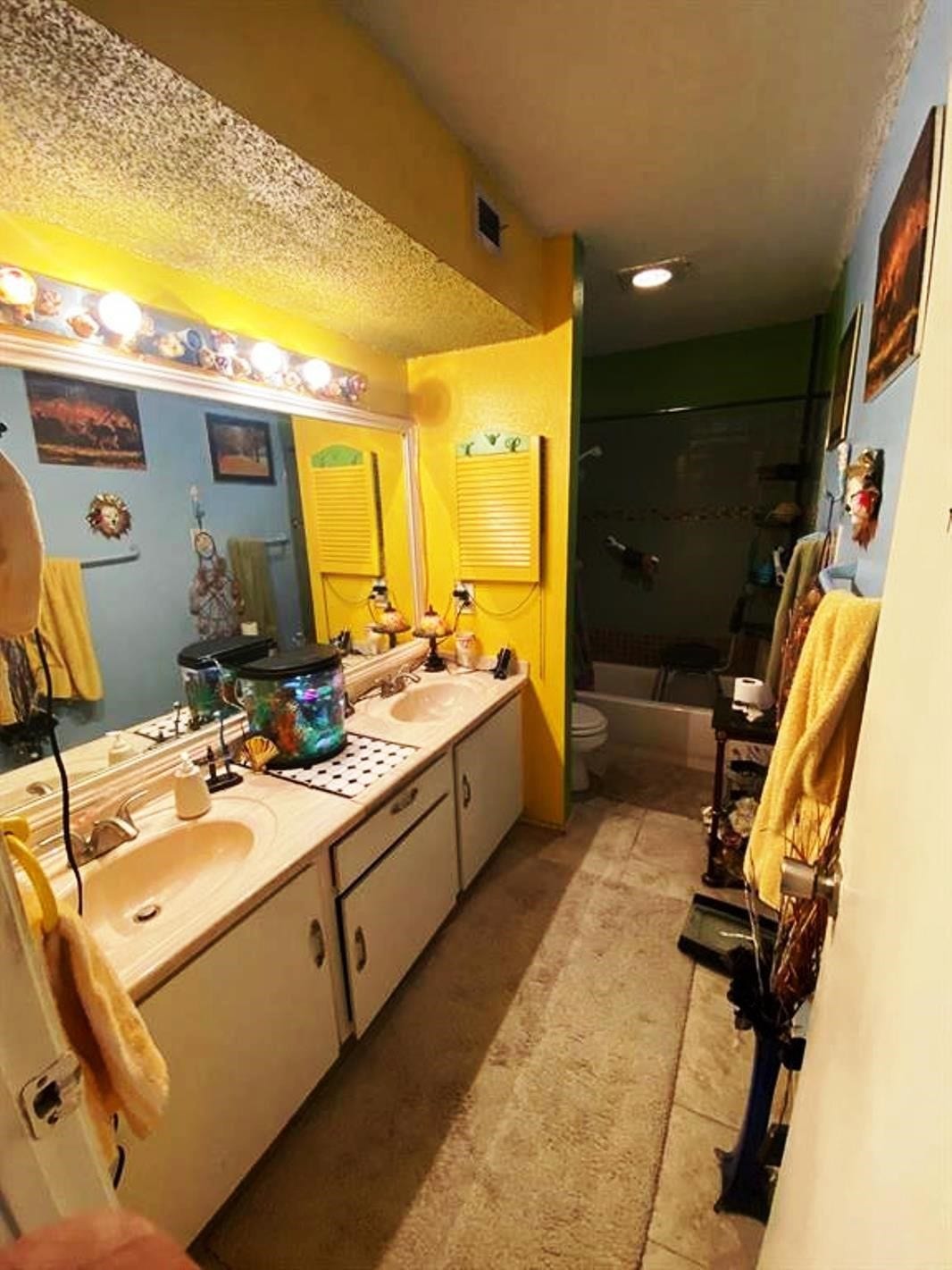 10049 Westpark Drive, #136, Houston, TX 77042 This bathroom features vibrant yellow and blue walls, dual sinks with a large mirror, and ample lighting. It includes a shower-tub combo and has quirky decorative elements, creating a unique and colorful atmosphere.