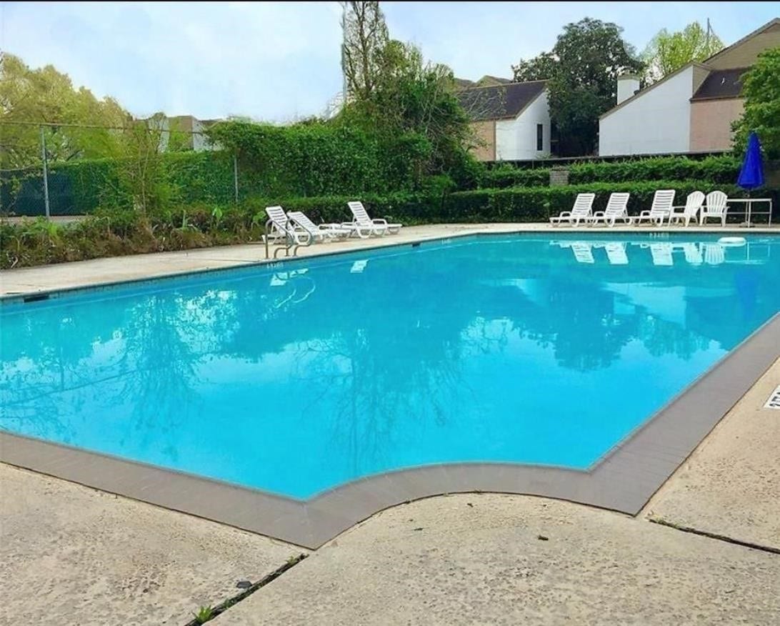10049 Westpark Drive, #136, Houston, TX 77042 This photo features a spacious outdoor swimming pool surrounded by a concrete deck, with several lounge chairs for relaxation. It's set against a backdrop of greenery and nearby houses, offering a serene and inviting atmosphere for residents.