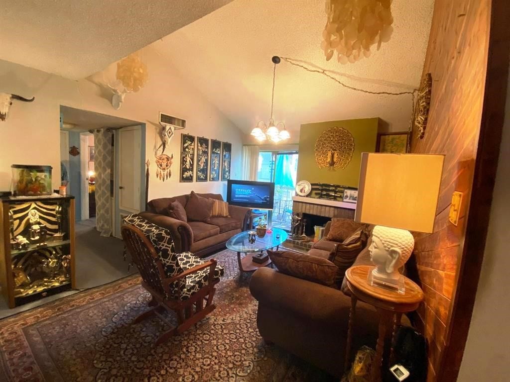10049 Westpark Drive, #136, Houston, TX 77042 This cozy living room features vaulted ceilings, warm lighting, and a mix of eclectic decor. A comfortable seating area is centered around a glass coffee table, with a fireplace as a focal point. The space is accented with art pieces and a plush rug, offering a welcoming and unique atmosphere.