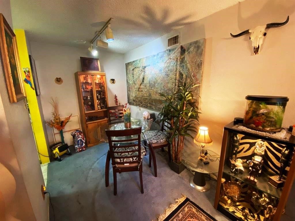 10049 Westpark Drive, #136, Houston, TX 77042 Cozy dining area with unique decor, featuring a glass table and chairs, art pieces, and display cabinets. The room has a warm ambiance with soft lighting and decorative items like a fish tank and wall-mounted skull.