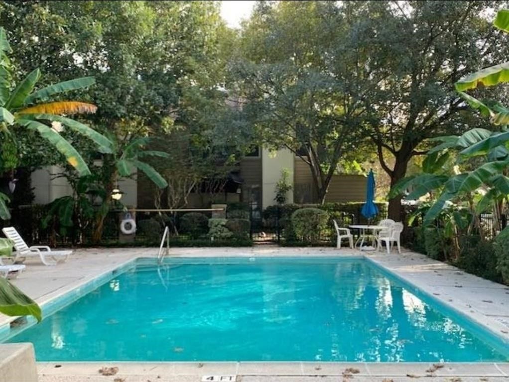 10049 Westpark Drive, #136, Houston, TX 77042 This photo showcases a serene backyard with a well-maintained pool surrounded by lush greenery. There's a seating area with a table and chairs, perfect for relaxing or entertaining.
