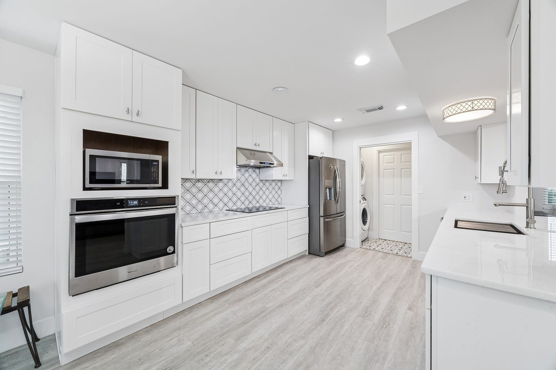 1814 Tiki Drive, Tiki Island, TX 77554 This sleek, modern kitchen boasts pristine white cabinetry, state-of-the-art stainless steel appliances, and an elegant tile backsplash, offering a bright and inviting space perfect for culinary creativity.