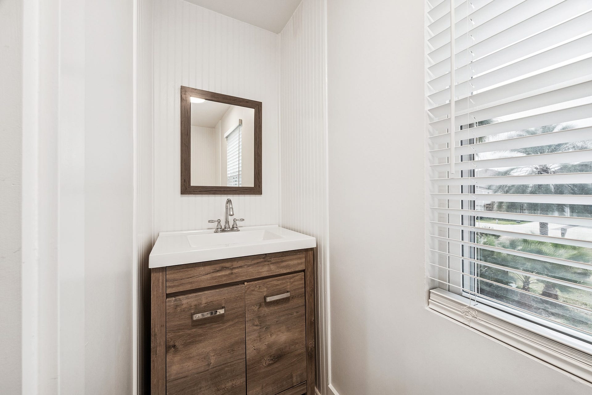 1814 Tiki Drive, Tiki Island, TX 77554 This inviting 1/2 bath powder room boasts a sleek vanity with warm wood accents and a bright window, perfect for welcoming guests with style.