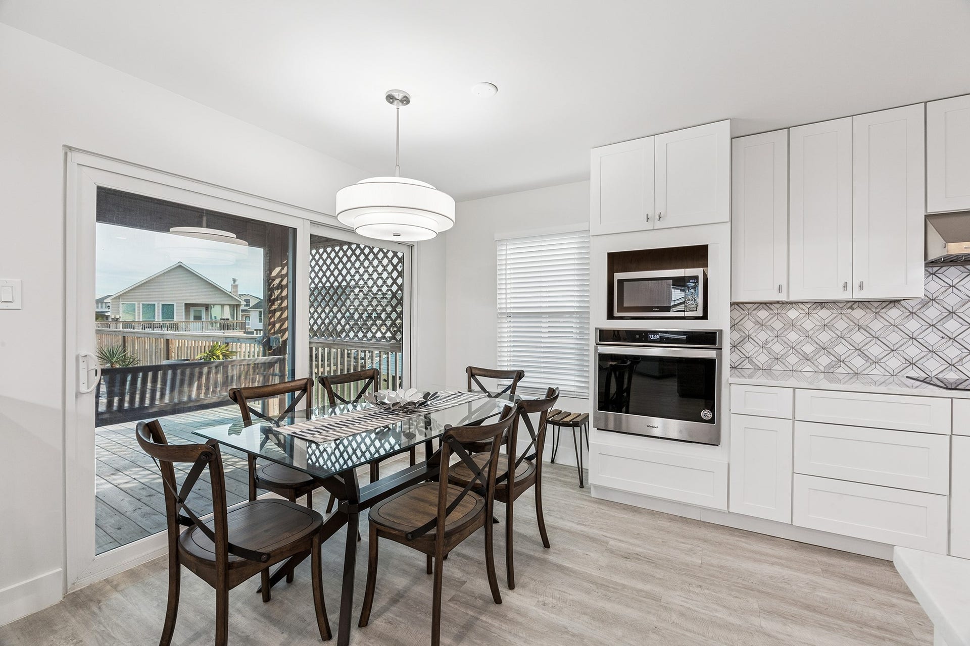 1814 Tiki Drive, Tiki Island, TX 77554 Discover a bright and inviting dining space seamlessly connected to a modern kitchen, featuring elegant cabinetry and an expansive glass door opening to a serene backyard deck, perfect for entertaining and family gatherings.