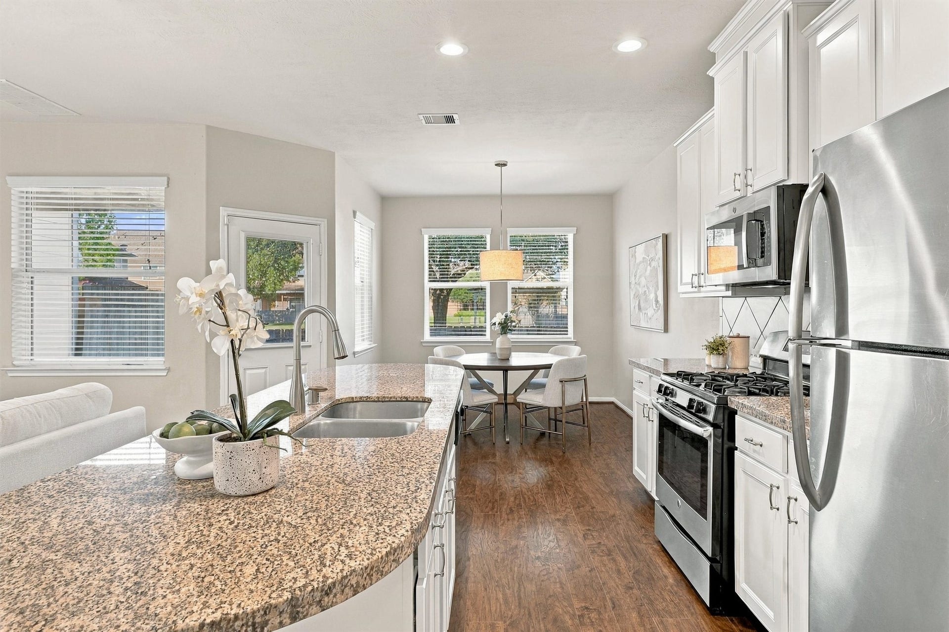 8323 Lamond Lane, Houston, TX 77095 This view of the kitchen shows off the gorgeous natural light that flows through the space. Wood laminate floors, Sherwin Williams paint, white cabinets, recessed lighting, and an elegant drum shade pendant in the dining room all create a luxurious feel.