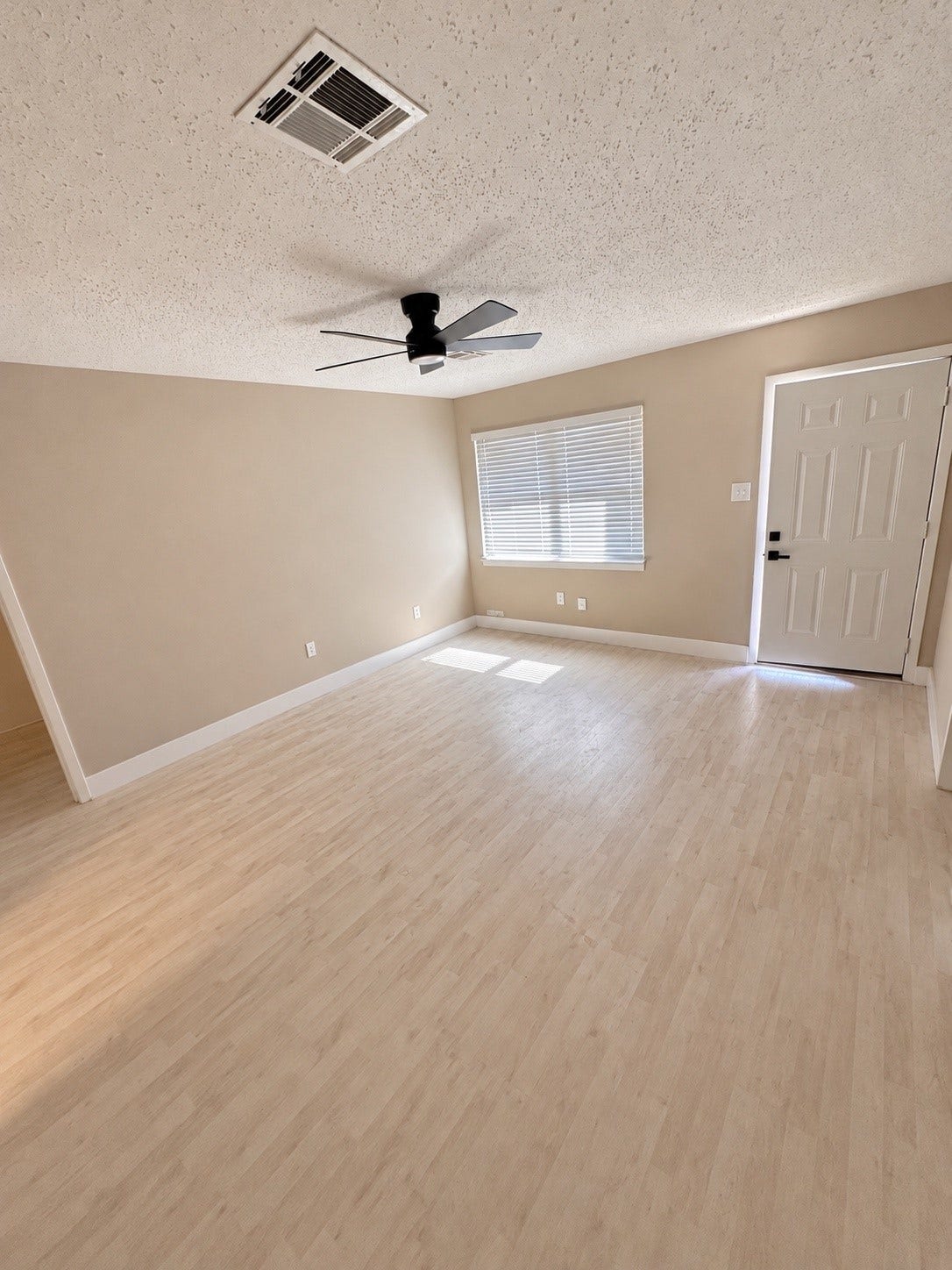 Bright and airy room featuring light wood flooring, a modern ceiling fan, and ample natural light through a large window.