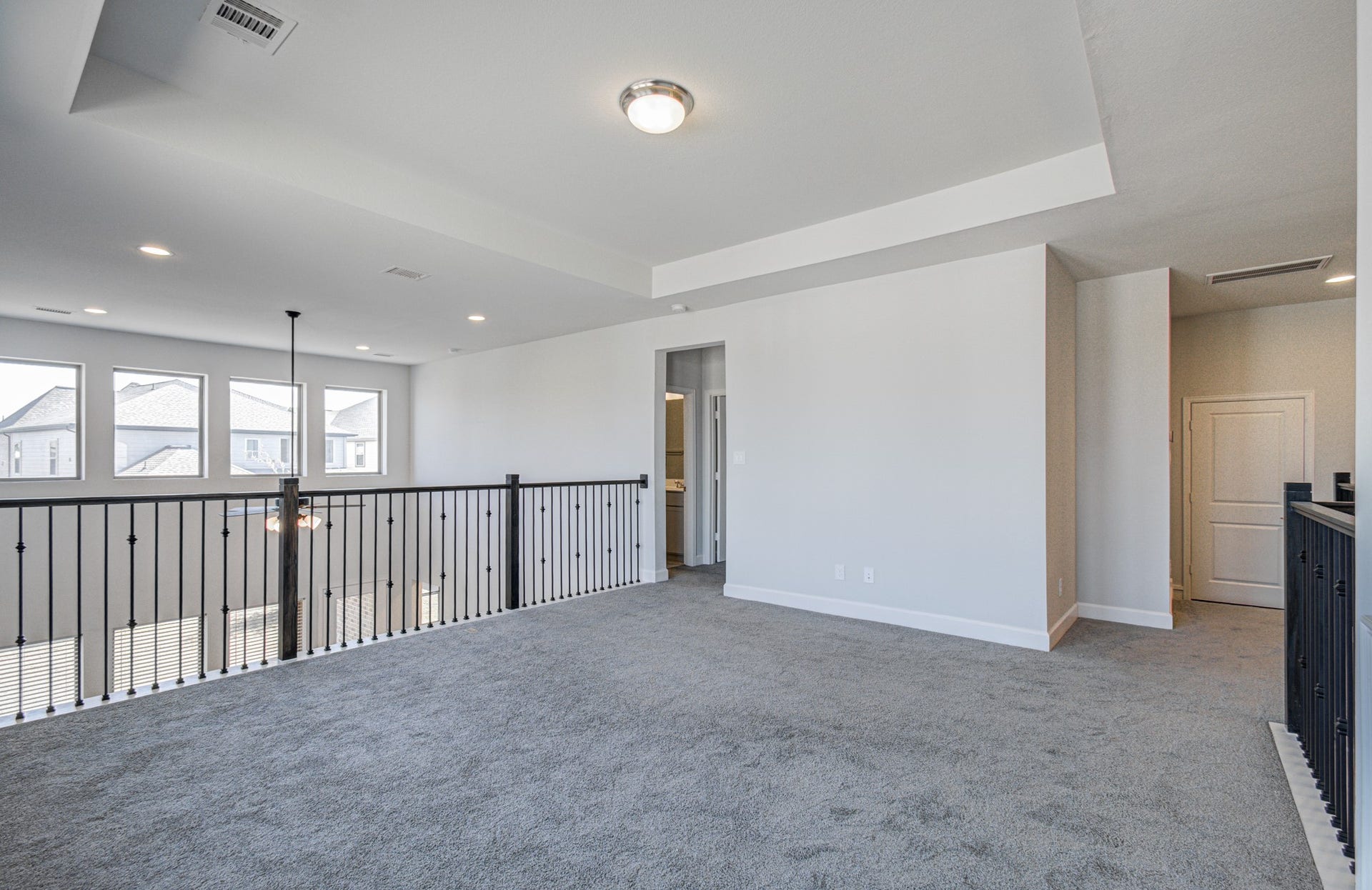 Plush carpeting, modern railing, and ample natural light from large windows, offering a versatile space for relaxation or entertainment.
