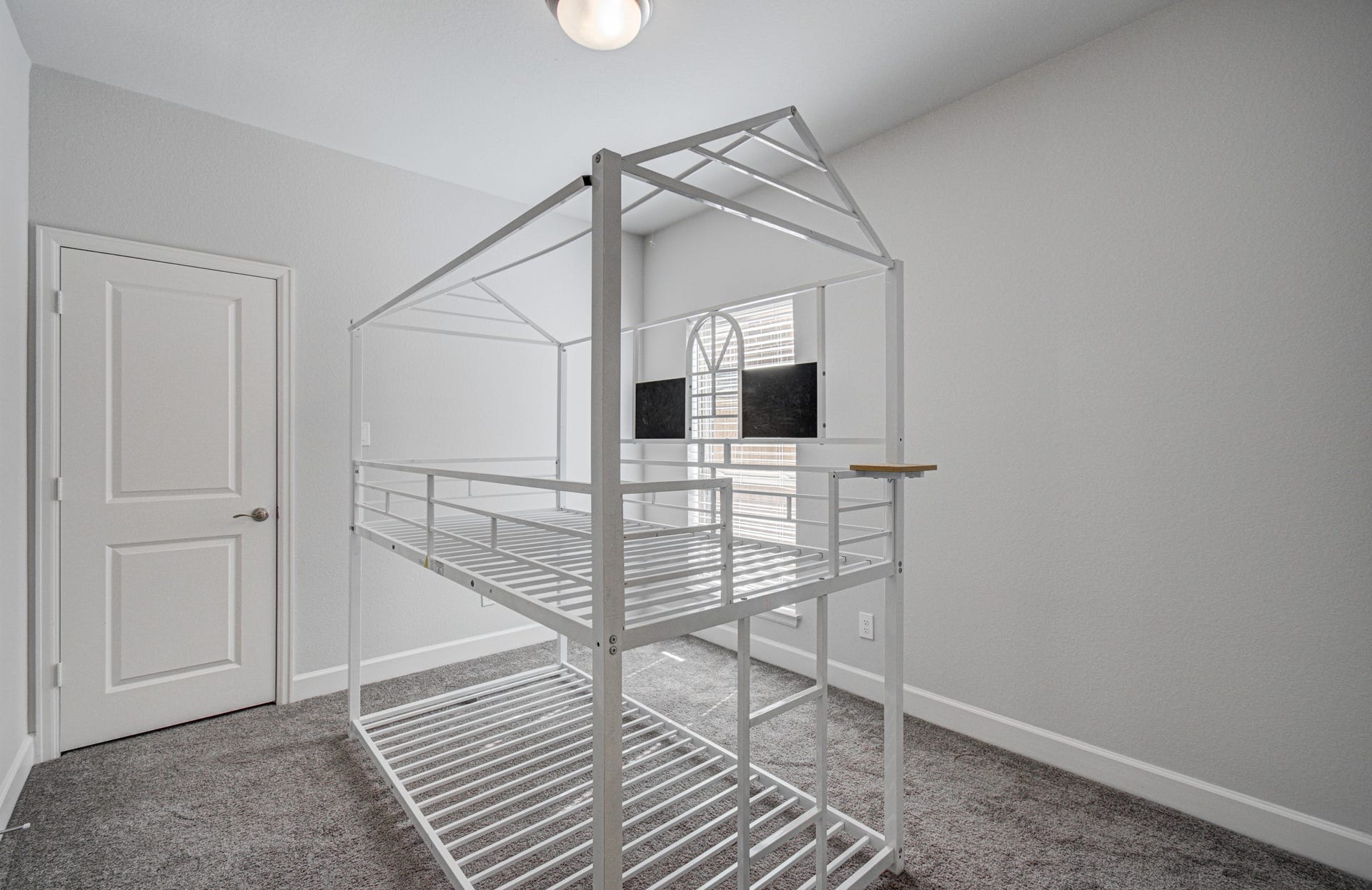 A cozy secondary bedroom located on the first floor features soft carpeting and ample natural light from a large window.