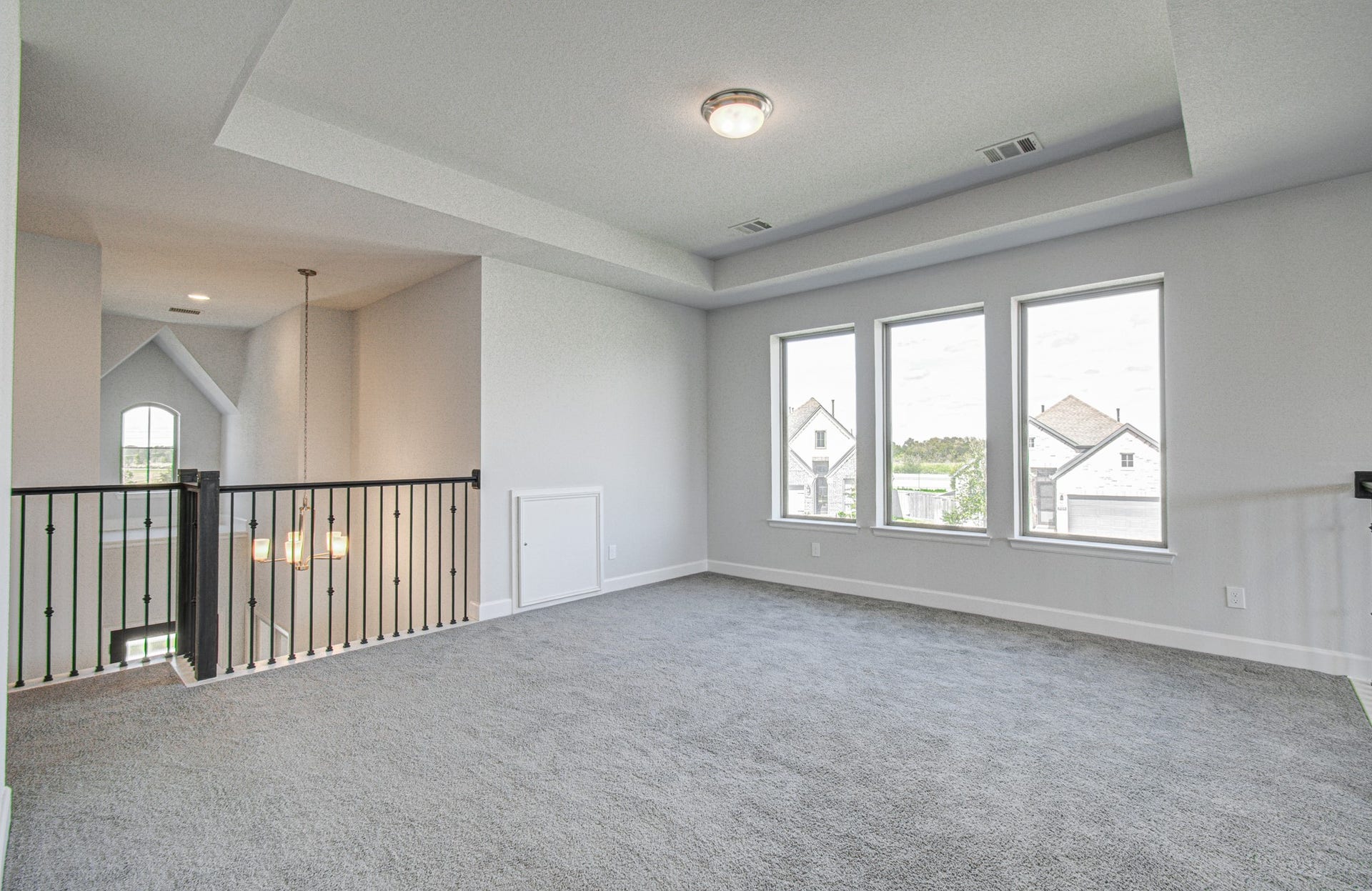 Bright and spacious upstairs loft game room featuring large windows, plush carpeting, and a stylish tray ceiling.