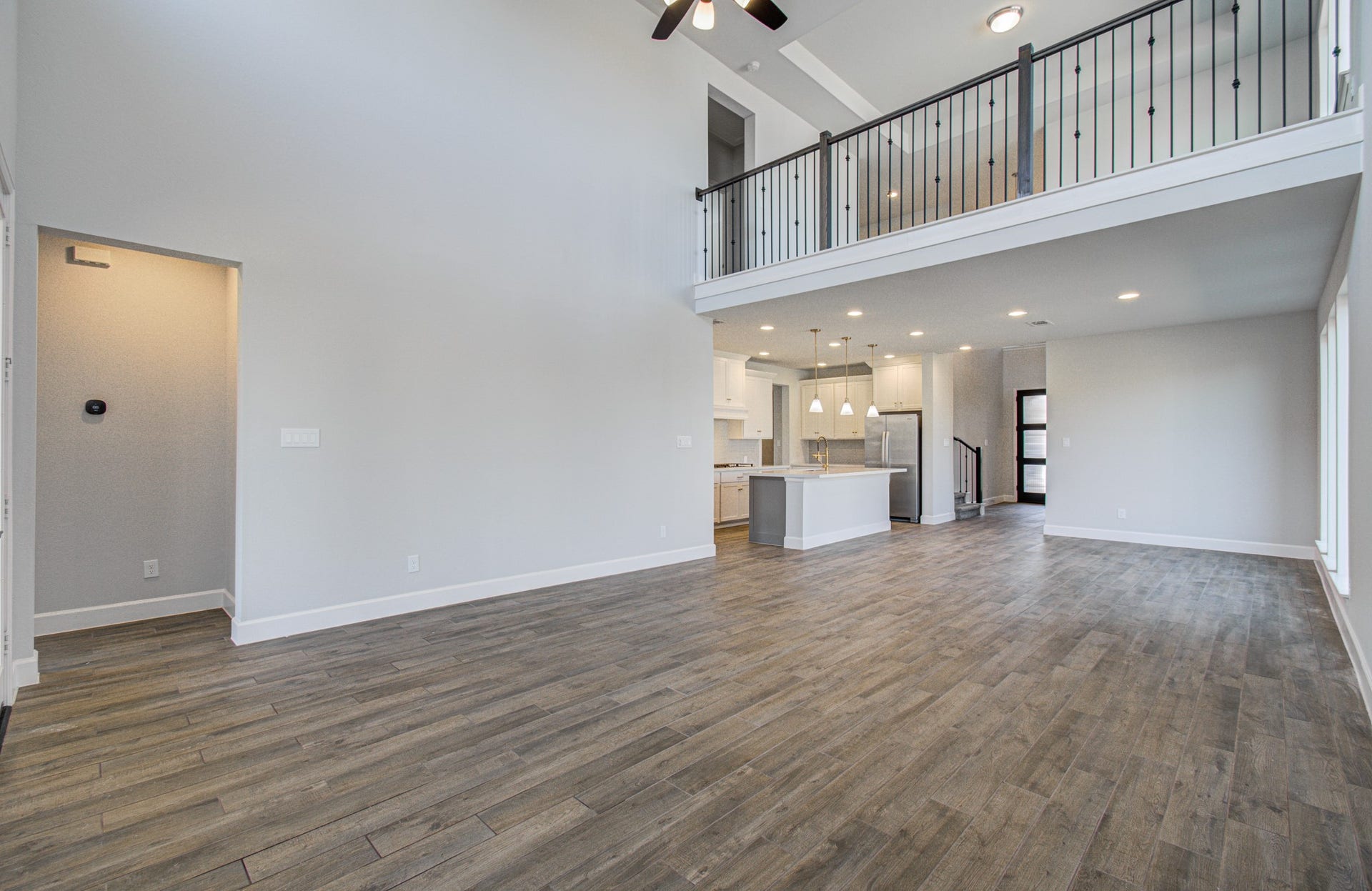 Spacious open-concept living area with high ceilings, featuring elegant flooring and a modern kitchen with stainless steel appliances. A stylish loft overlooks the space, enhancing the home's airy feel.