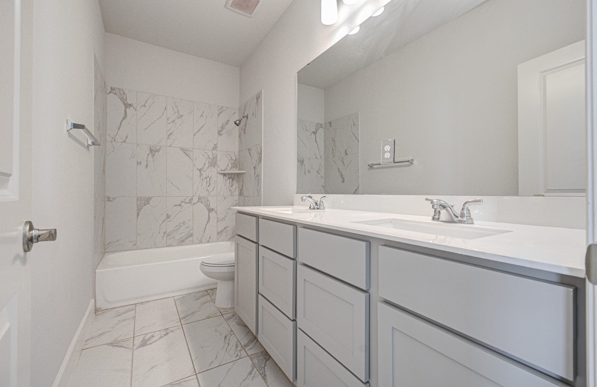 Elegant third bathroom with a double vanity, sleek white countertops, and modern fixtures. The shower features stylish marble-patterned tiles for a sophisticated touch.