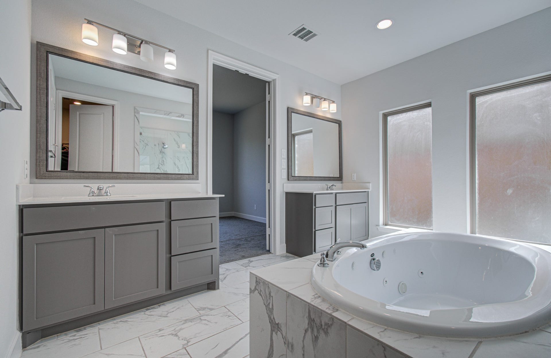 Luxurious primary bathroom featuring a spacious jetted tub, dual vanities with elegant mirrors, and abundant natural light from frosted windows.