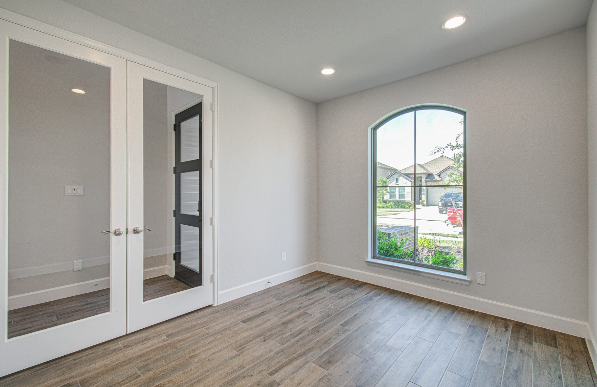 Bright and inviting office/flex room with elegant flooring, a large arched window providing ample natural light, and stylish glass double doors for a modern touch.