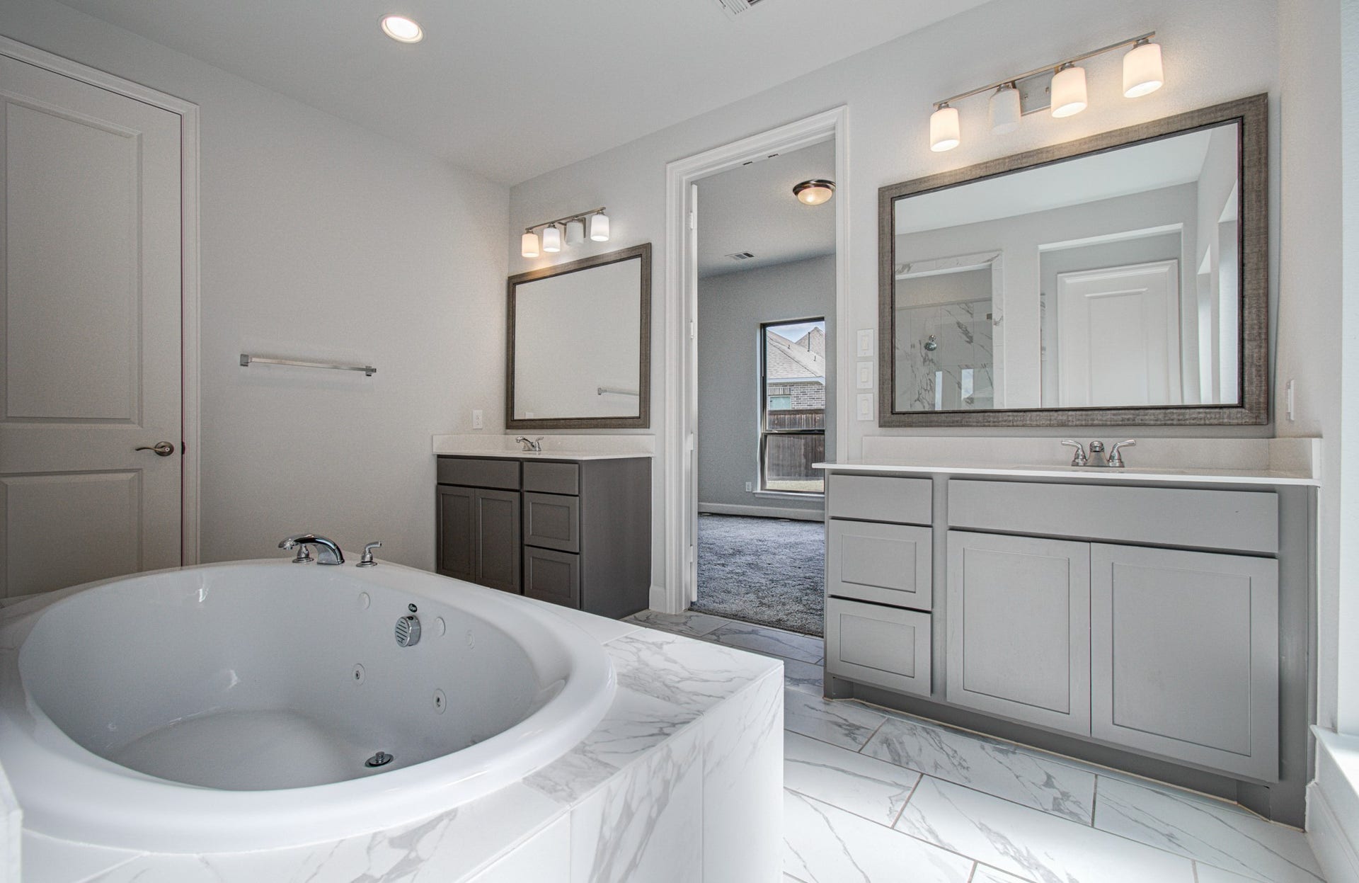 Luxurious bathroom featuring a spacious jetted tub, dual vanities with elegant lighting, and modern cabinetry, creating a serene and stylish retreat.