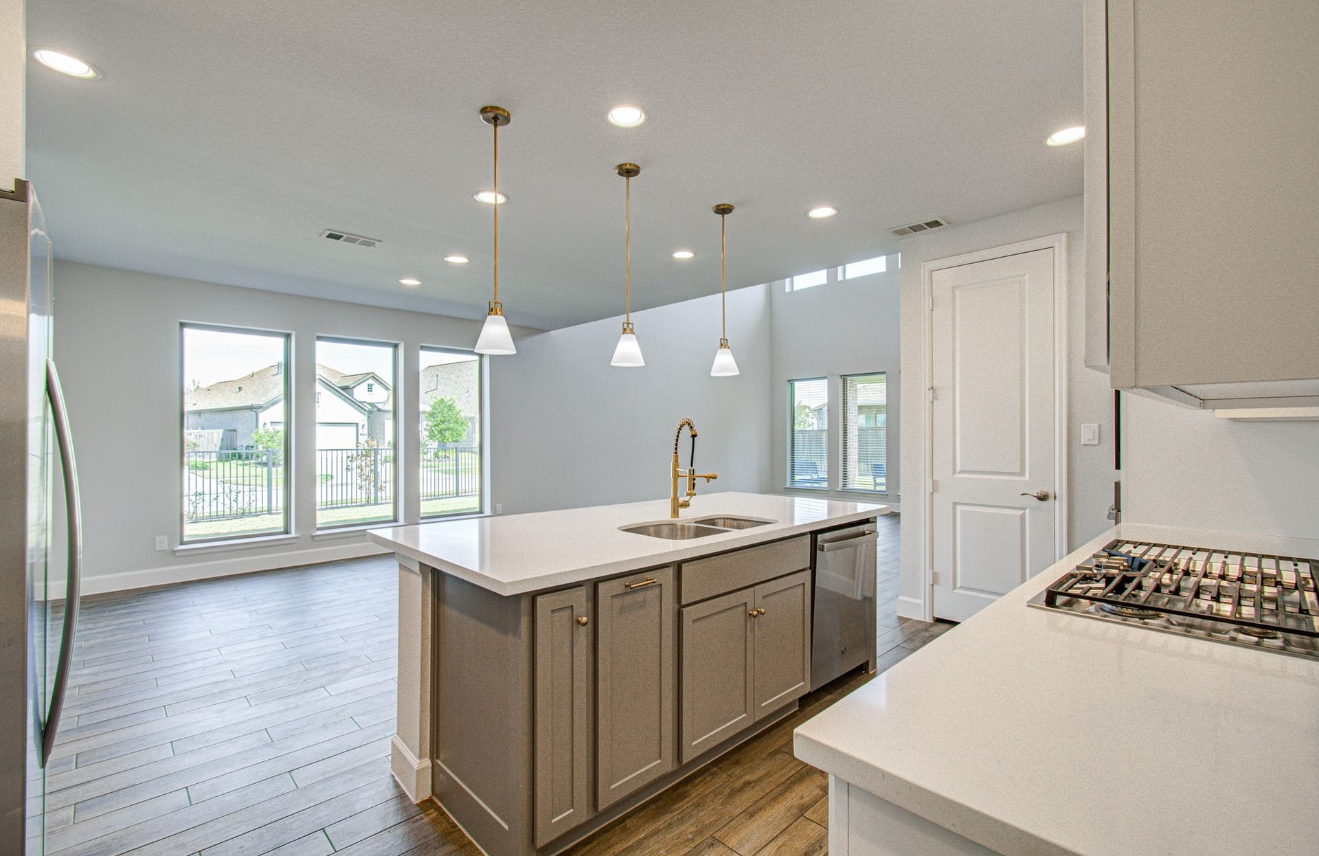Bright and modern kitchen featuring a spacious island with a sink, elegant pendant lighting, stainless steel appliances, and ample natural light from large windows.