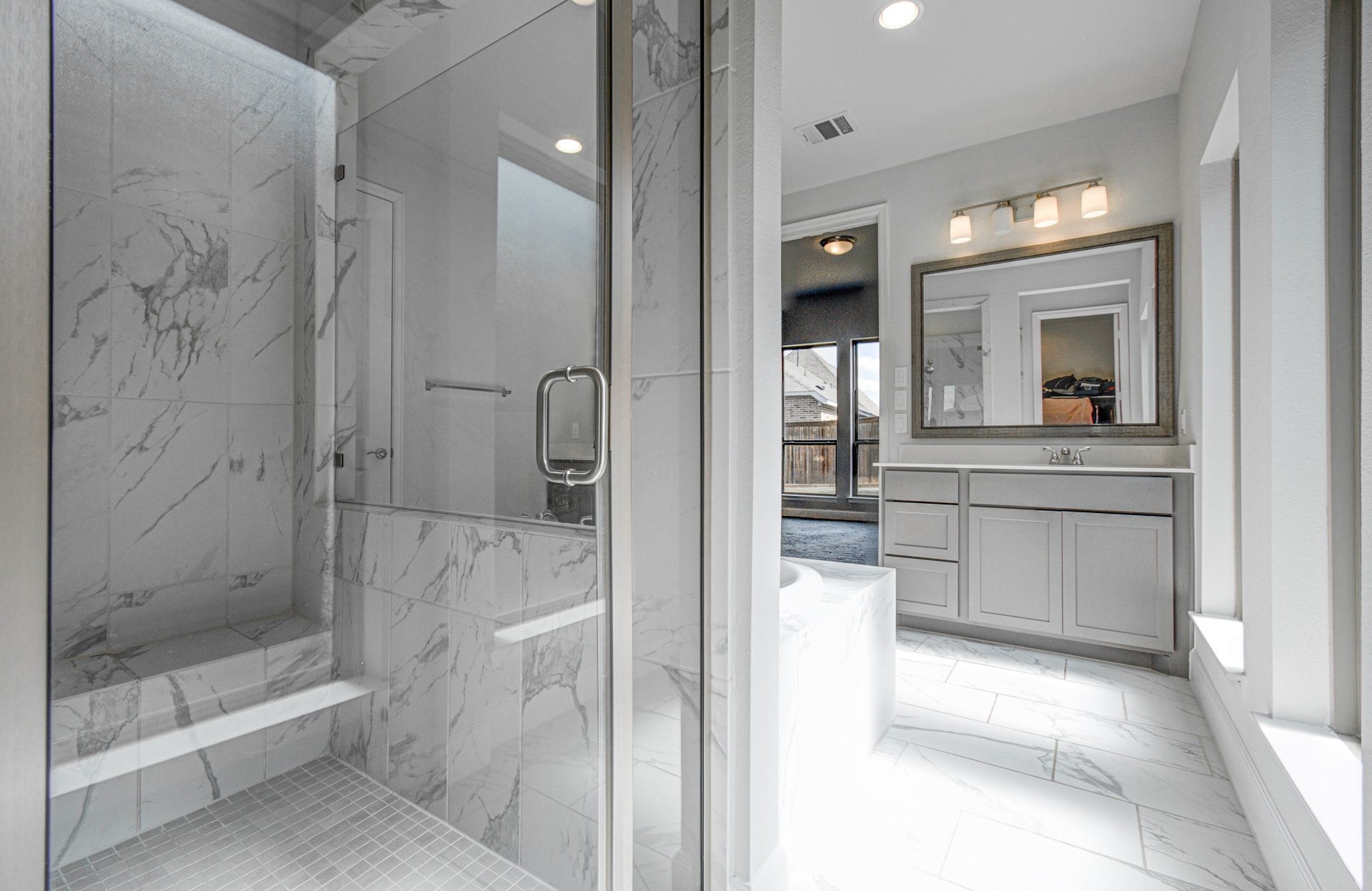 Elegant primary bathroom featuring a spacious glass-enclosed marble shower, modern vanity with framed mirror, and abundant natural light.
