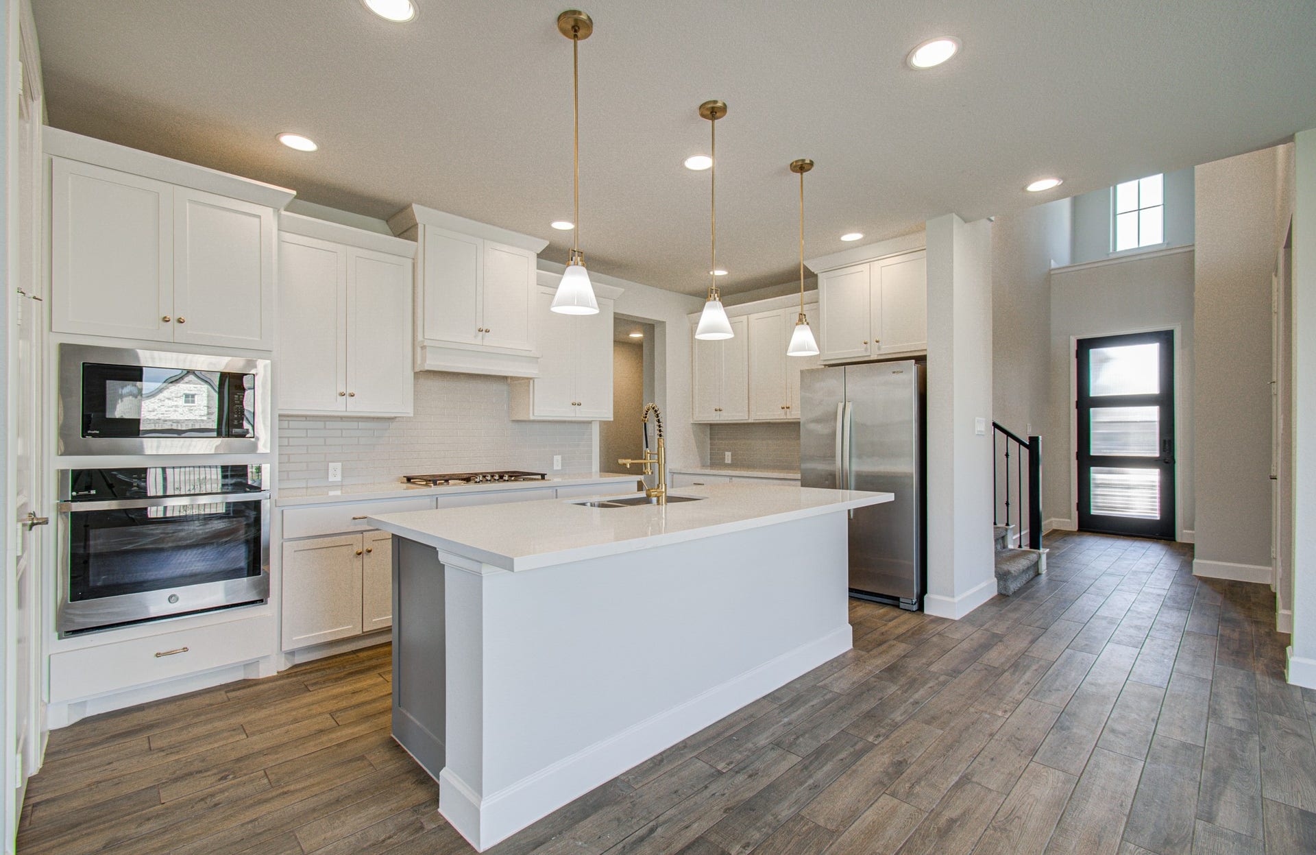 A modern kitchen featuring sleek white cabinetry, stainless steel appliances, and a spacious island with pendant lighting, complemented by elegant wood-look flooring and an open, airy layout.