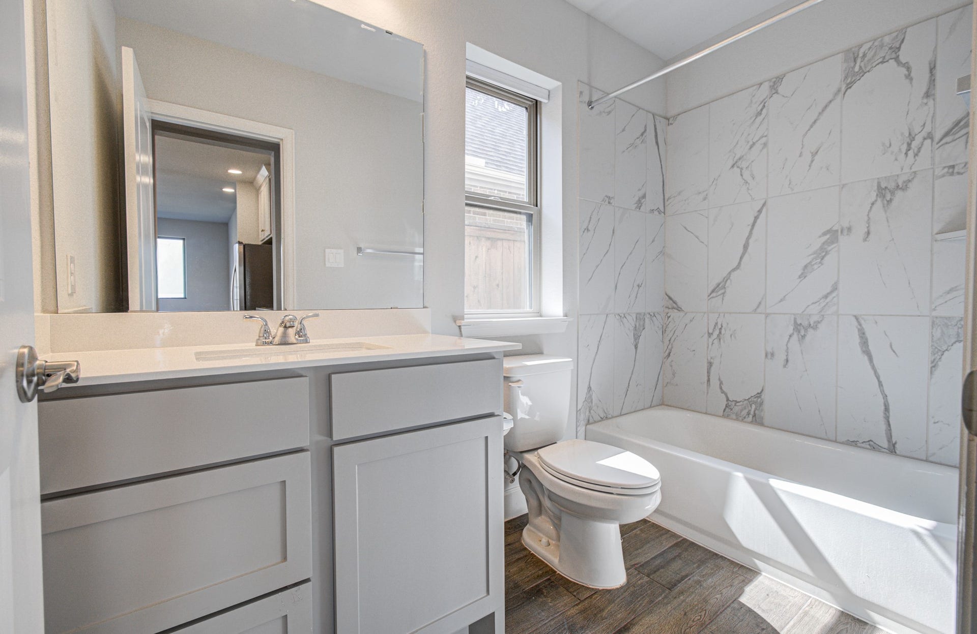 Sleek secondary bathroom located on the first floor with modern fixtures, featuring a marble look-tiled shower and tub, a large vanity with ample storage, and a window for natural light.