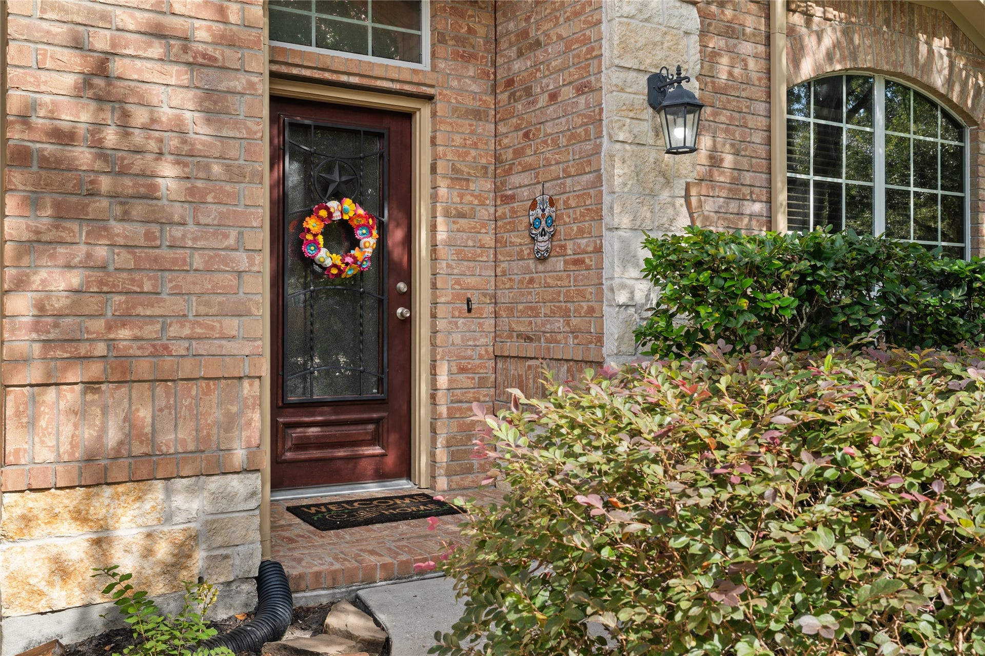 20184 Bitter Root Drive, Porter, TX 77365 Charming brick entryway features a welcoming door adorned with a colorful wreath, complemented by a decorative lantern and lush greenery.