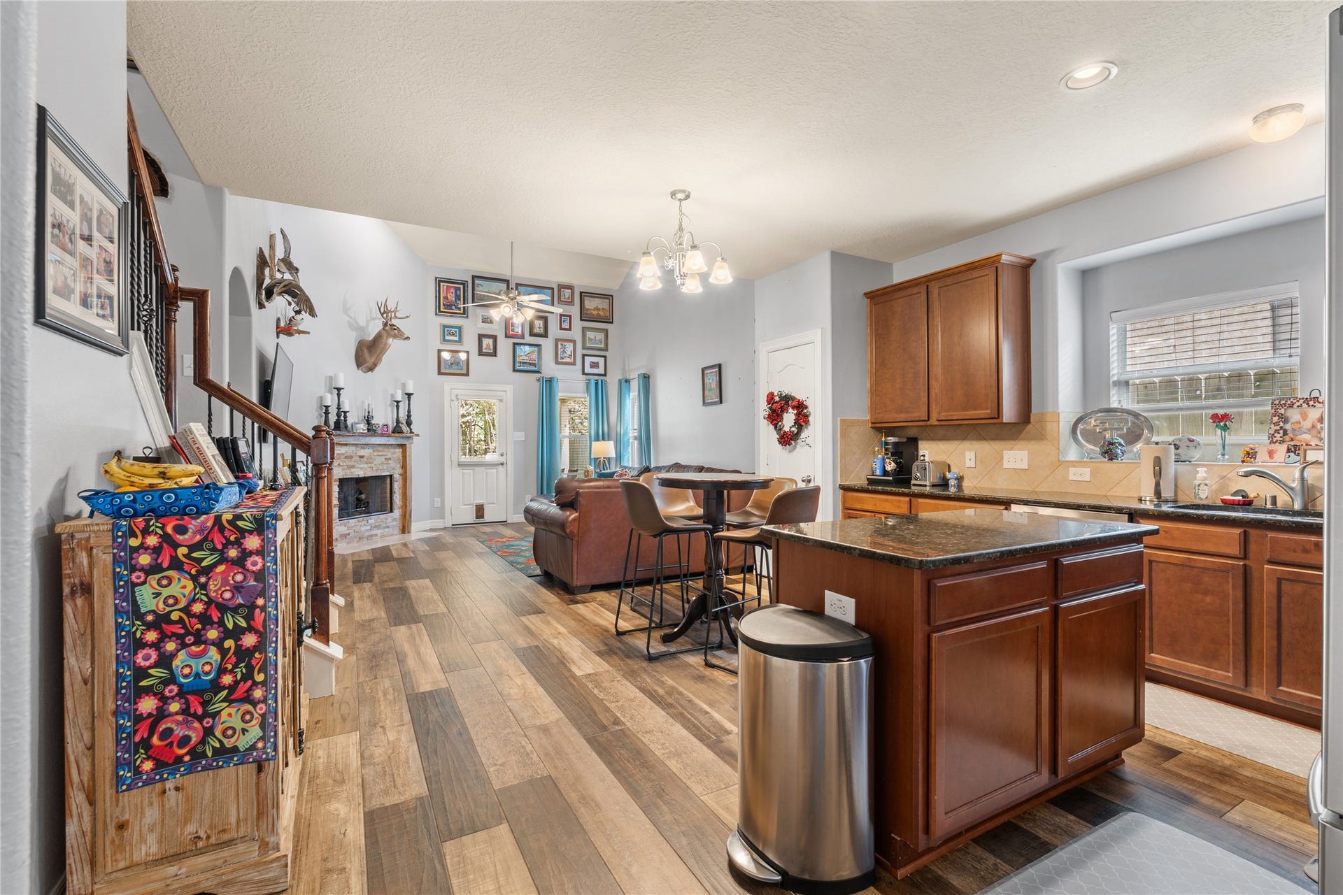 20184 Bitter Root Drive, Porter, TX 77365 Spacious open-concept living area with warm wood flooring, a cozy stone fireplace, and a modern kitchen featuring granite countertops and rich cabinetry.