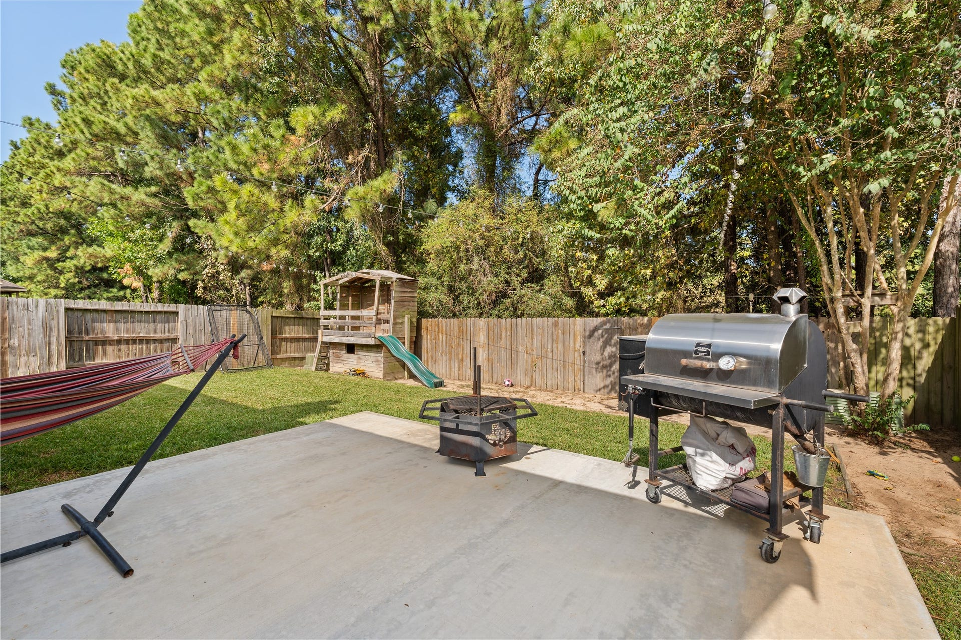 20184 Bitter Root Drive, Porter, TX 77365 Spacious backyard with a concrete patio, perfect for grilling and relaxation, featuring a hammock and a play area with a slide, surrounded by lush greenery for privacy.