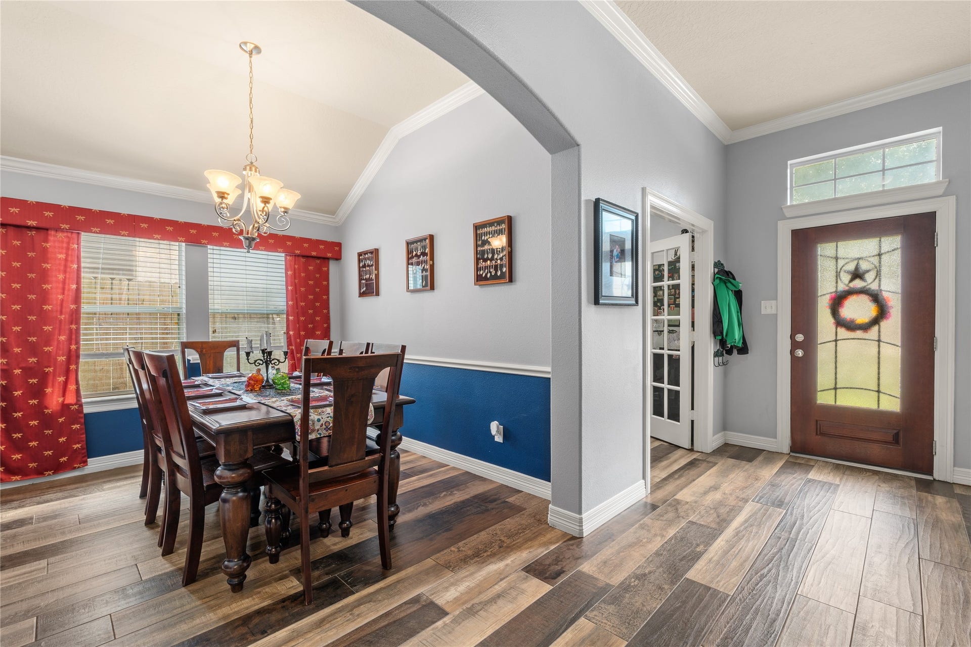 20184 Bitter Root Drive, Porter, TX 77365 Inviting dining area with elegant chandelier, rich wood flooring, and vibrant red curtains, seamlessly connected to a welcoming entryway with a decorative glass front door.