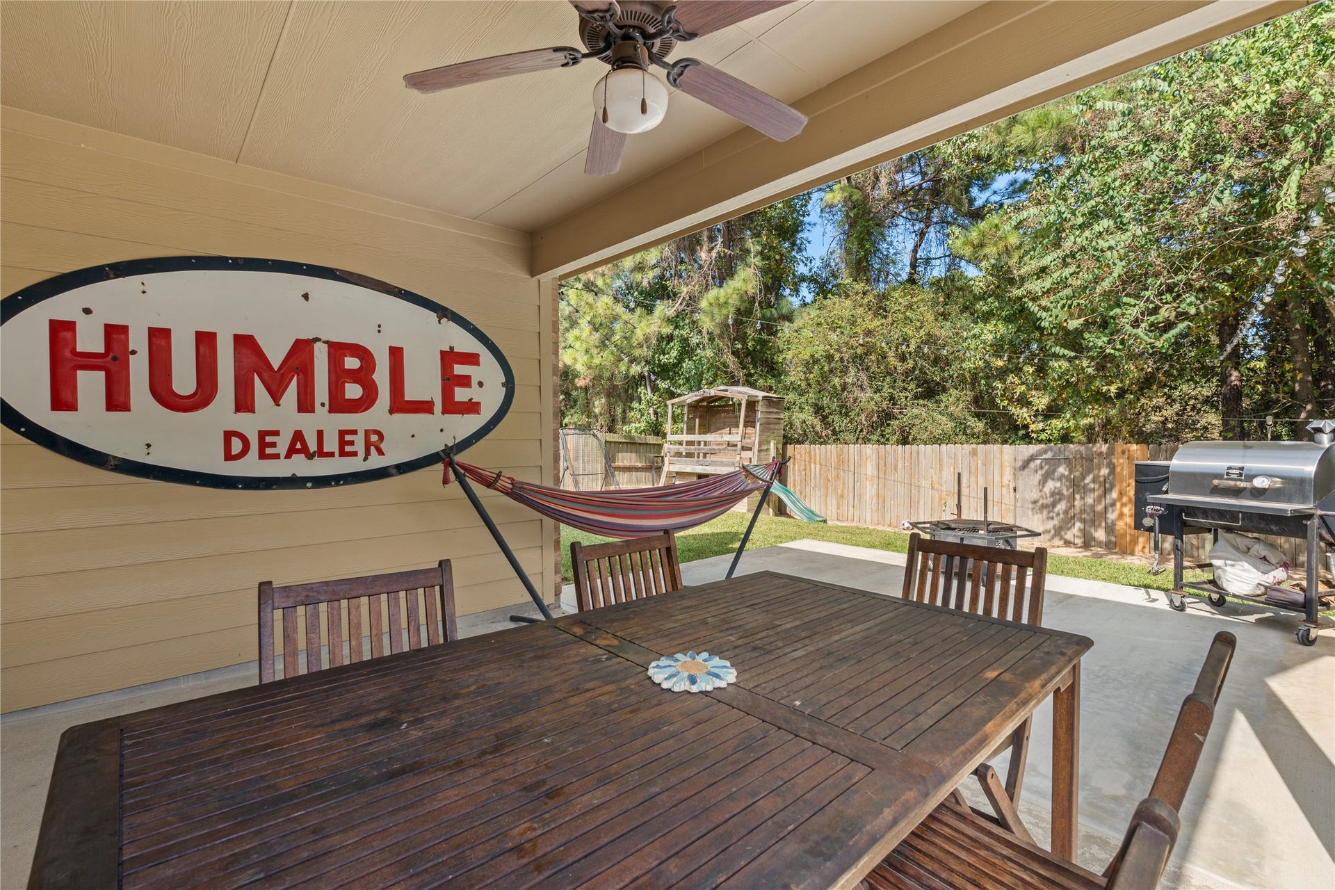 20184 Bitter Root Drive, Porter, TX 77365 Charming covered patio with a ceiling fan, perfect for outdoor dining and relaxation, featuring a hammock, BBQ grill, and views of the lush backyard.