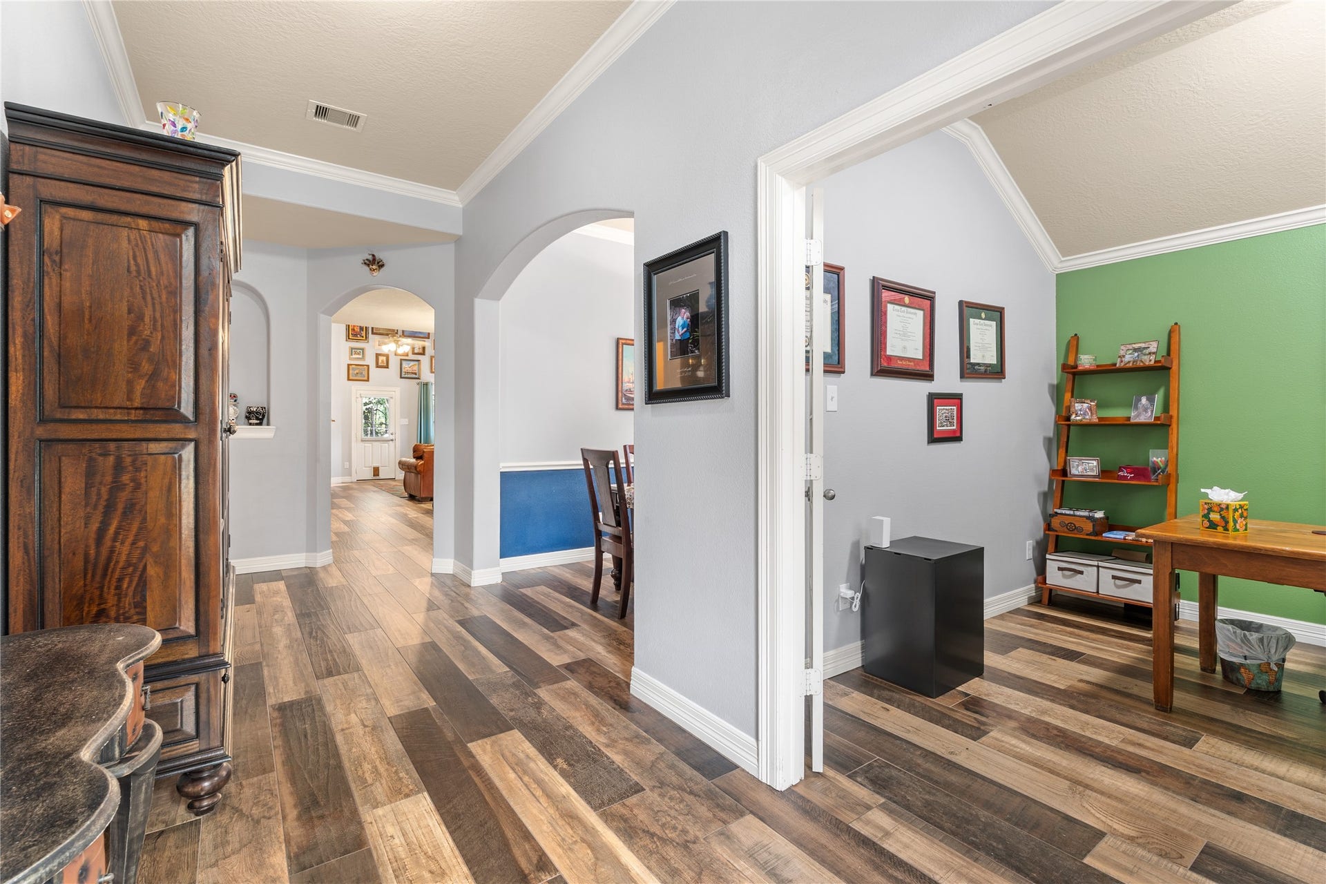 20184 Bitter Root Drive, Porter, TX 77365 Charming interior featuring elegant wood flooring, archways leading to a cozy living area, and a bright office space with vibrant green accents.