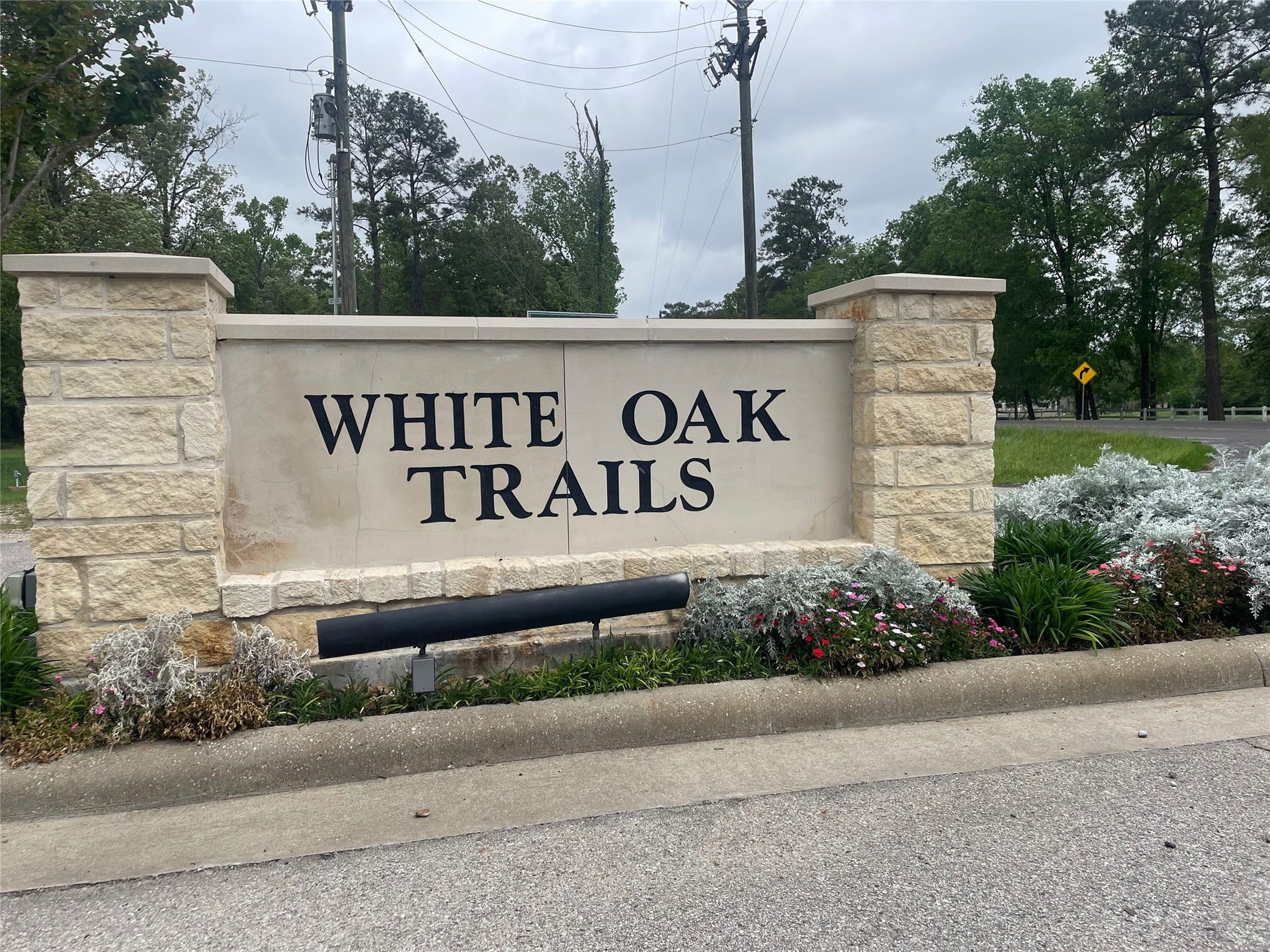 1230 Road 6324, Dayton, TX 77535 The photo shows the entrance to "White Oak Trails," featuring a stone sign with neatly landscaped surroundings and mature trees, creating a welcoming and natural ambiance for potential home buyers.