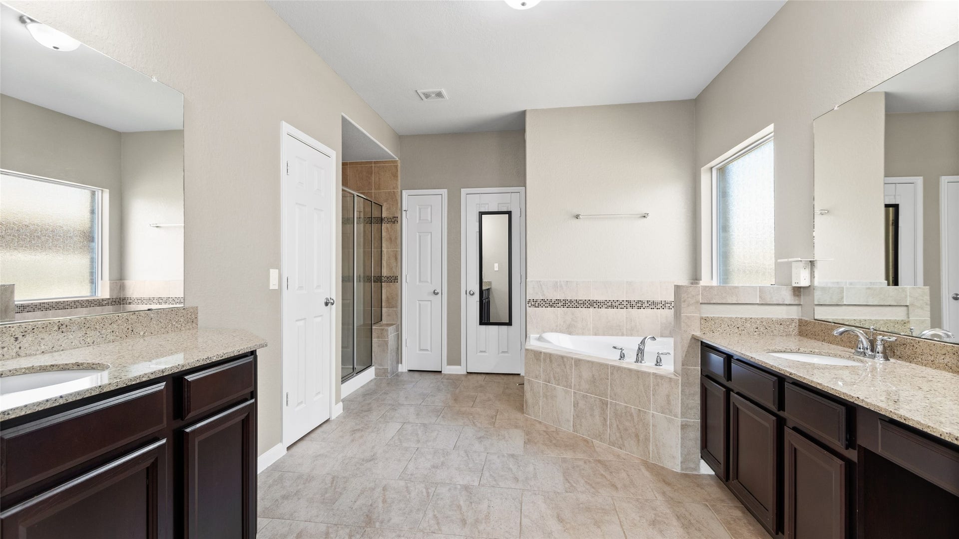 12106 Obsidian Lane, Mont Belvieu, TX 77535 Primary suite bathroom featuring beautiful slate stone flooring, dual large vanities with ample storage, a deep jetted tub, a separate stone and glass shower, and a spacious walk-in closet.