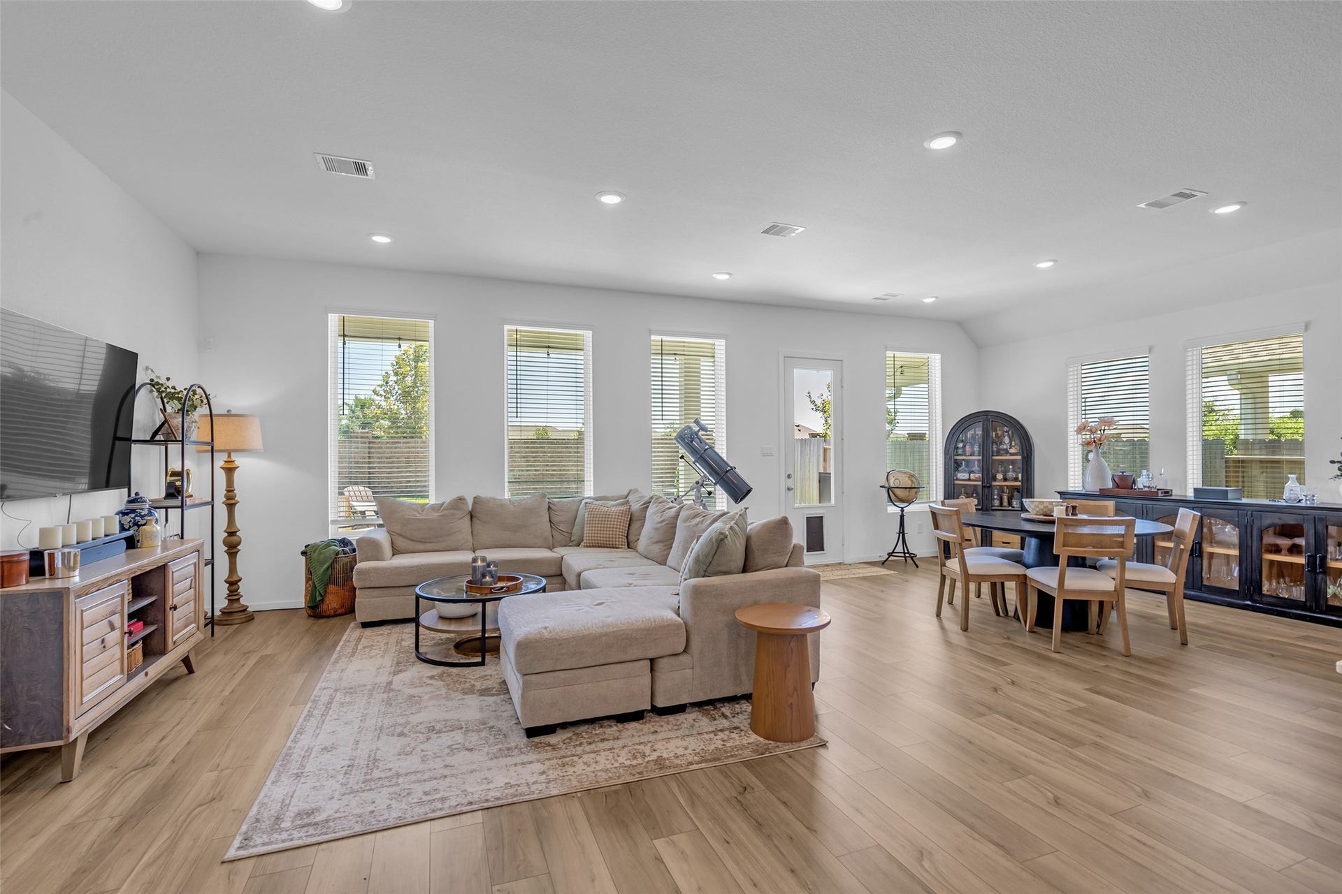 13213 Harbor Point Drive, Texas City, TX 77539 Spacious and bright open-concept living area featuring hardwood floors, large windows, and a cozy sectional sofa, seamlessly connected to a dining space with modern furnishings.