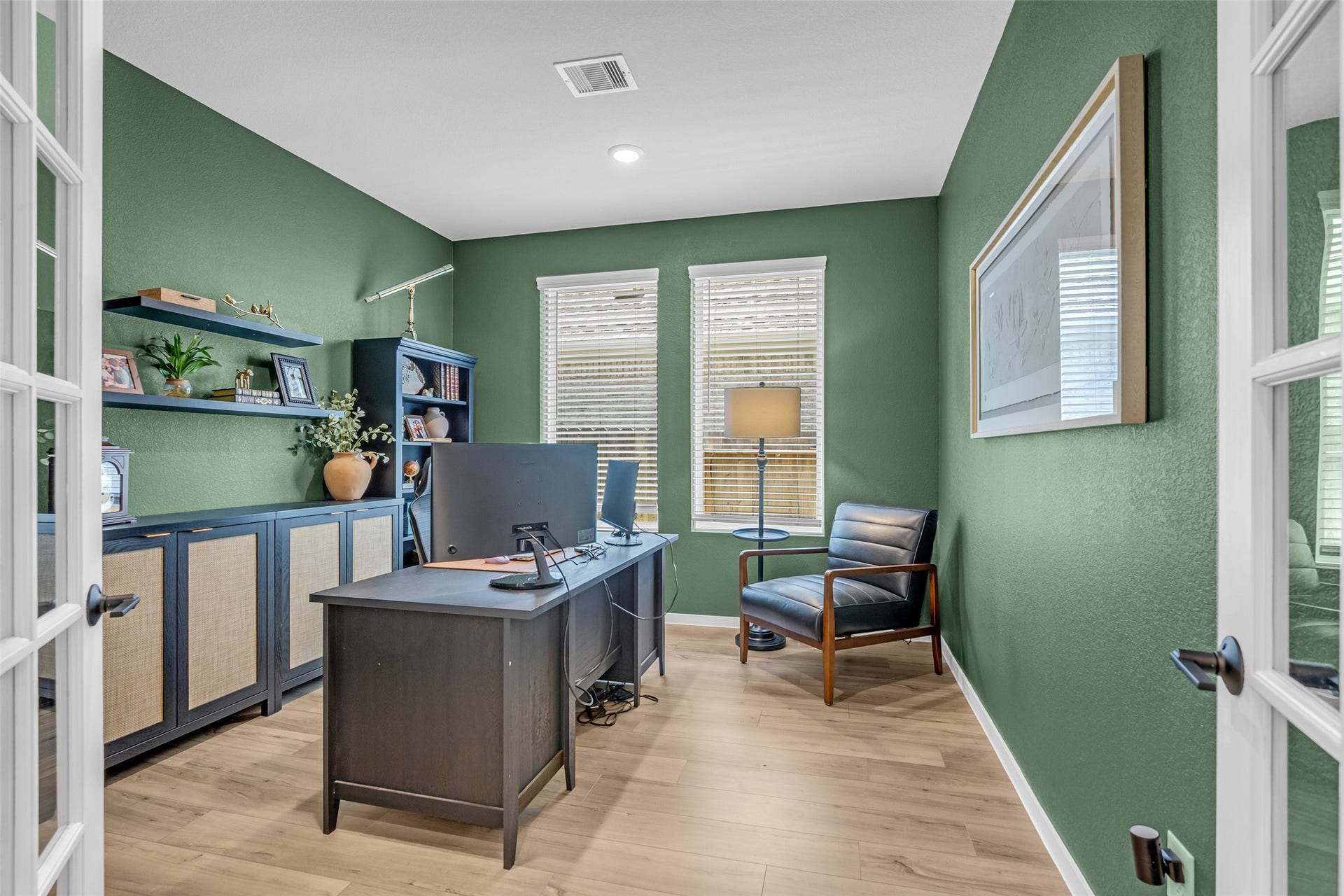 13213 Harbor Point Drive, Texas City, TX 77539 Elegant home office with rich green walls, featuring a sleek desk, cozy leather chair, ample natural light from two windows, and stylish built-in shelving for storage and decor.