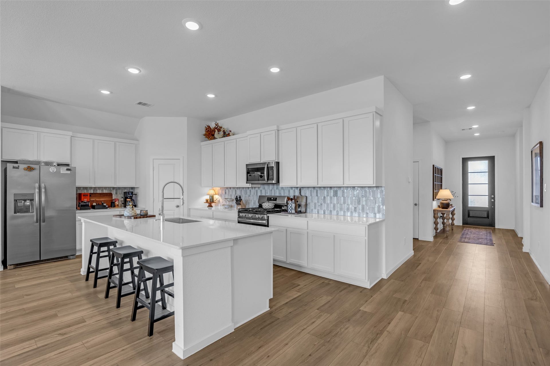 13213 Harbor Point Drive, Texas City, TX 77539 Sleek and modern kitchen with white cabinetry, stainless steel appliances, and a spacious island with seating, beautifully complemented by a stylish backsplash and warm wood flooring.