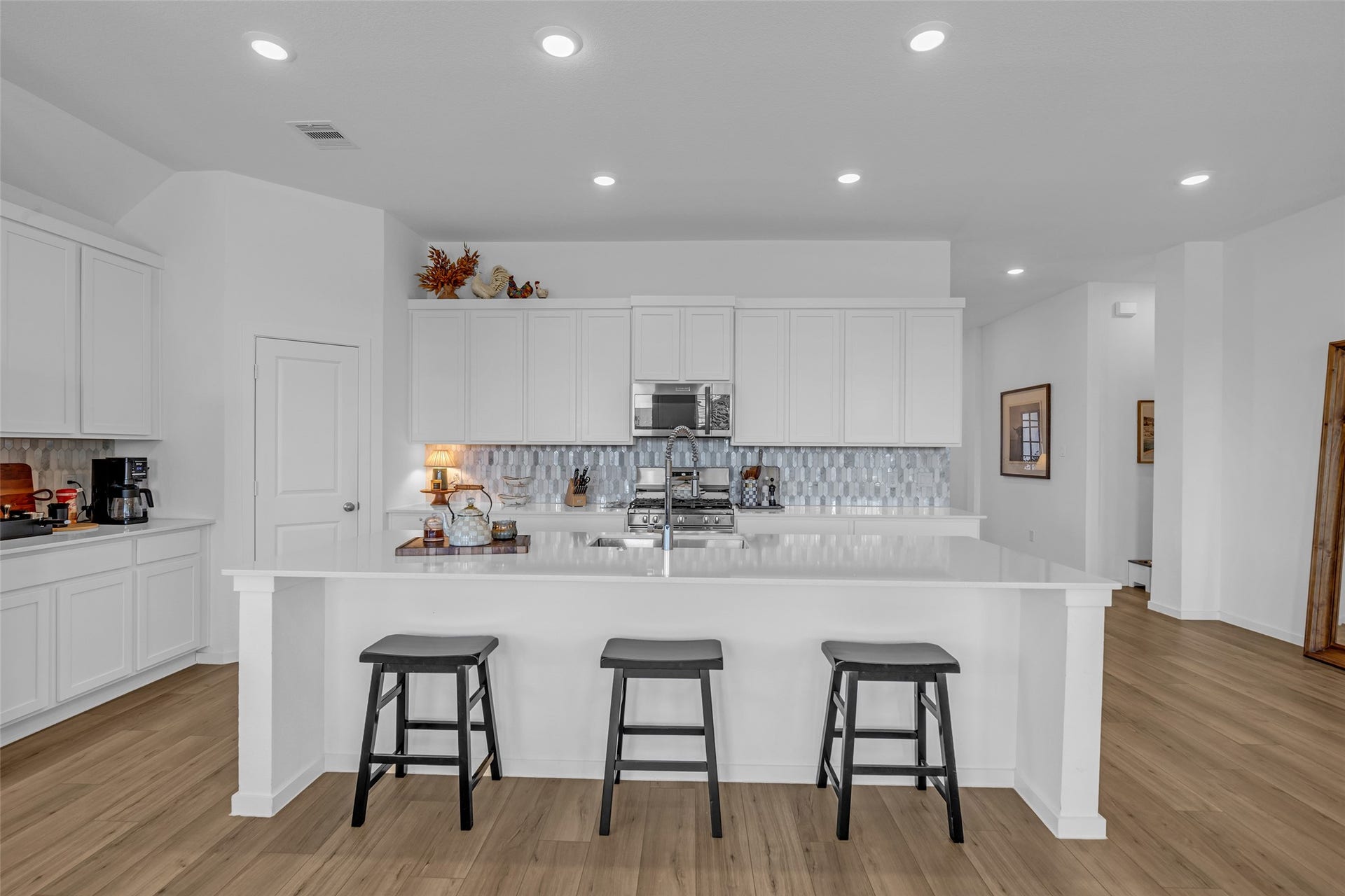 13213 Harbor Point Drive, Texas City, TX 77539 Experience the elegance of a bright, modern kitchen featuring sleek white cabinetry, a spacious island with seating, and stylish tile backsplash, all set against beautiful wood like flooring.
