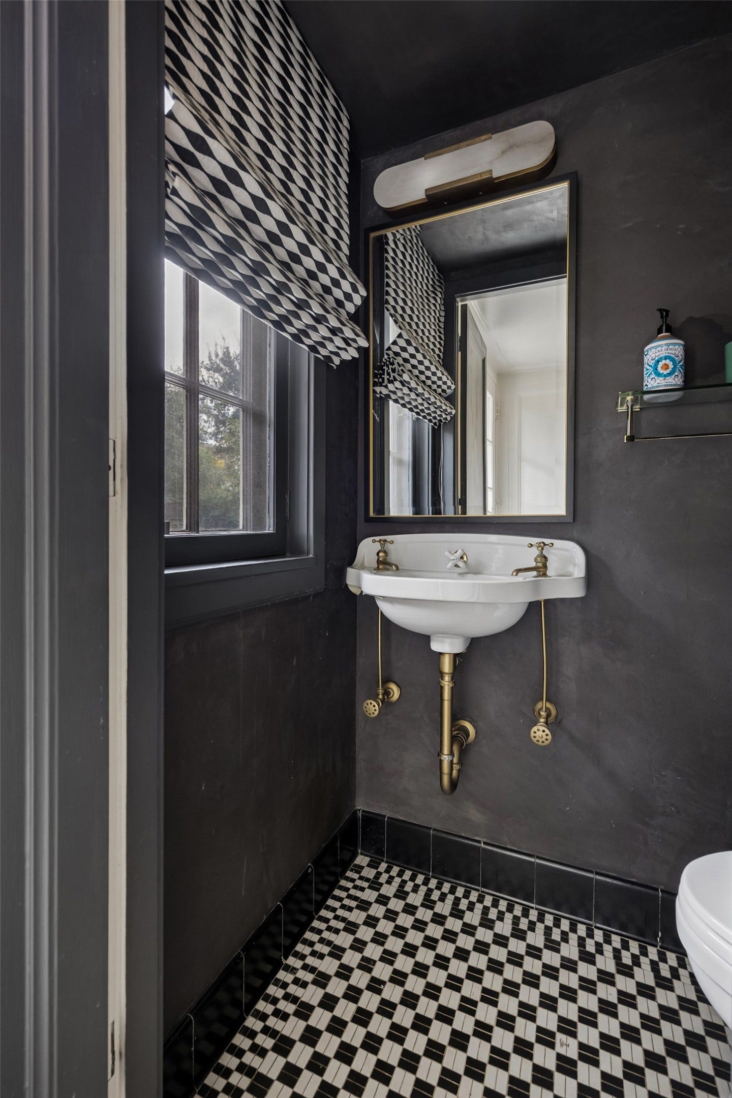 8 Courtlandt Place, Houston, TX 77006 A striking powder room makes a sophisticated statement with dramatic dark walls, geometric tile flooring and a vintage-inspired console sink with brass accents.