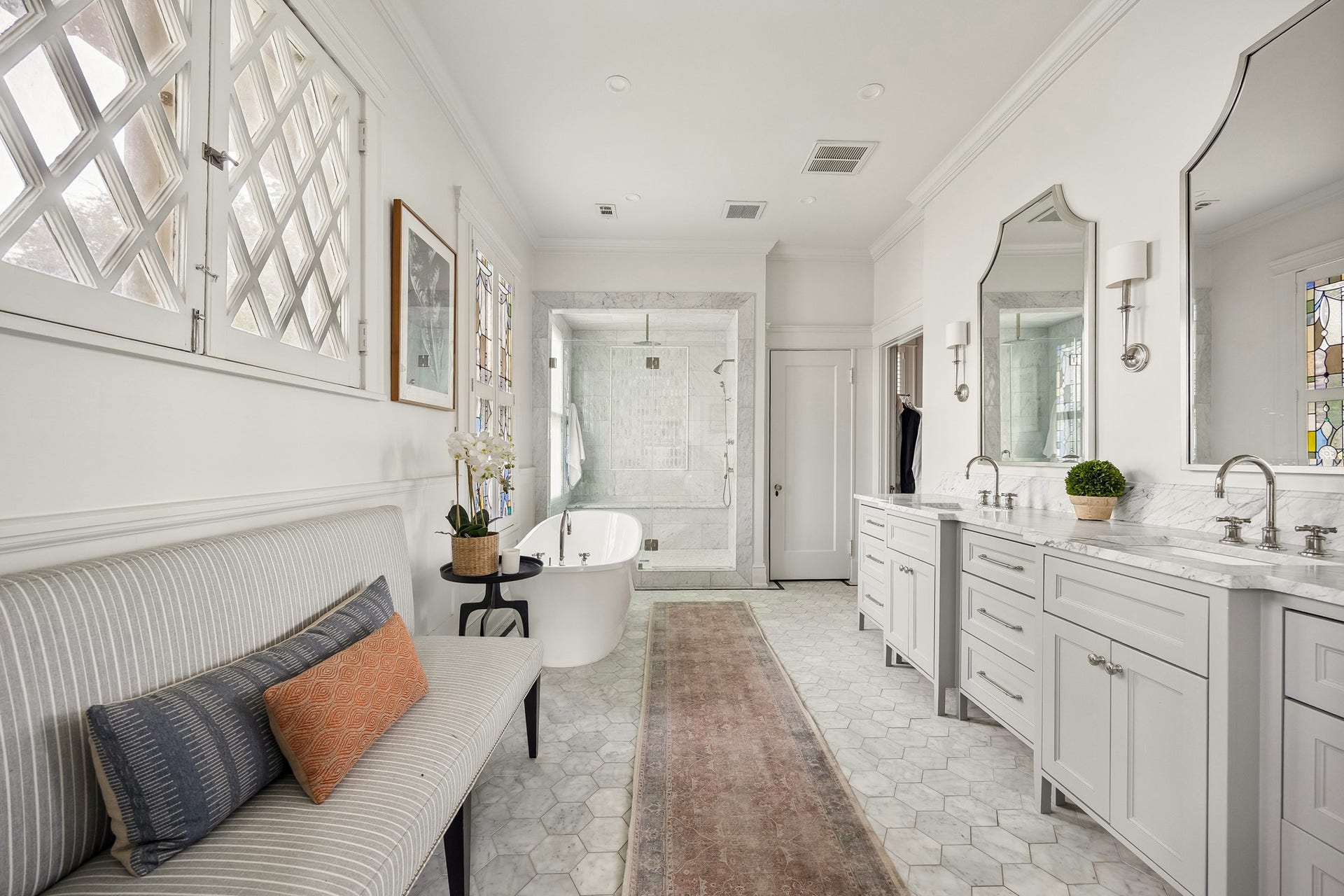 8 Courtlandt Place, Houston, TX 77006 A beautifully renovated primary bath features dual vanities, marble finishes, a freestanding soaking tub and an oversized glass-enclosed shower.