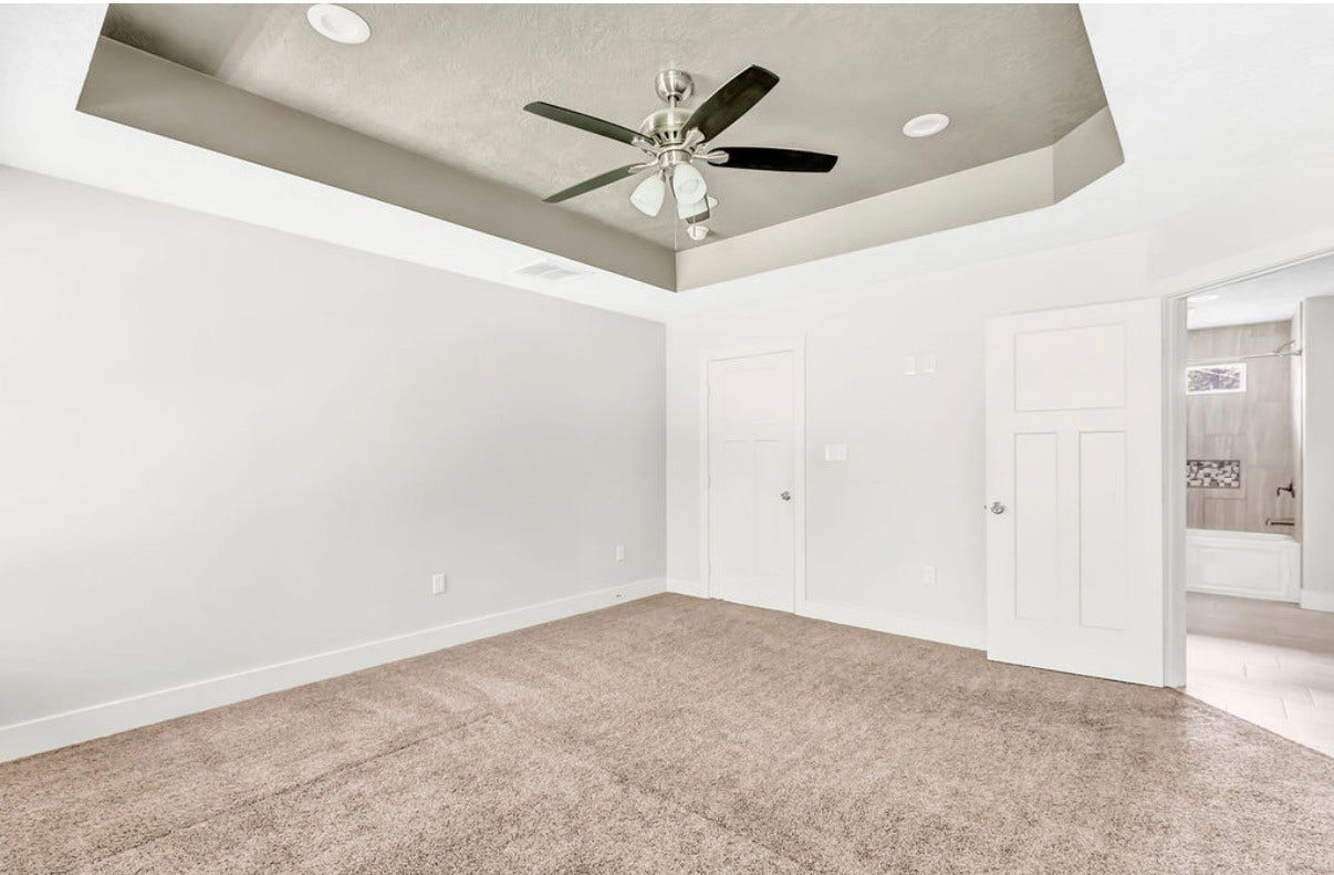 Spacious bedroom featuring a stylish tray ceiling with recessed lighting, a modern ceiling fan, and plush carpeting, leading to an ensuite bathroom.