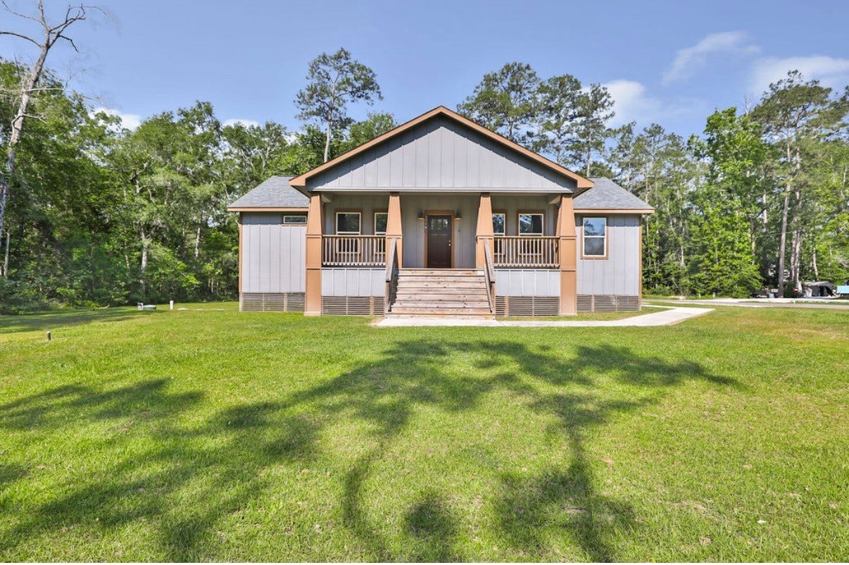Charming country-style home with a welcoming front porch, nestled in serene natural beauty.