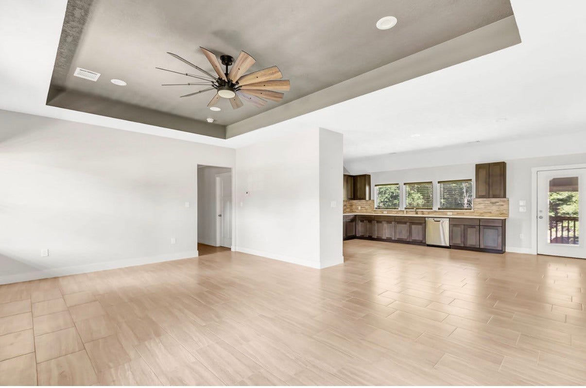 Discover the allure of a spacious open-concept living area showcasing sleek tile flooring, a modern ceiling fan, and a stylish kitchen with dark cabinetry and stainless steel appliances.