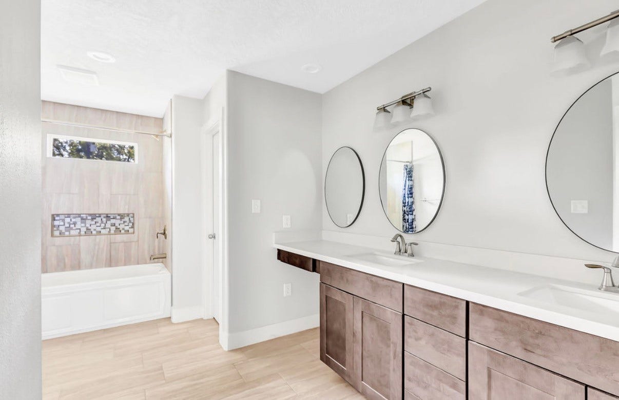 A bright and modern bathroom showcases a double vanity with elegant fixtures and a stylish bathtub enhanced by accent tile details.